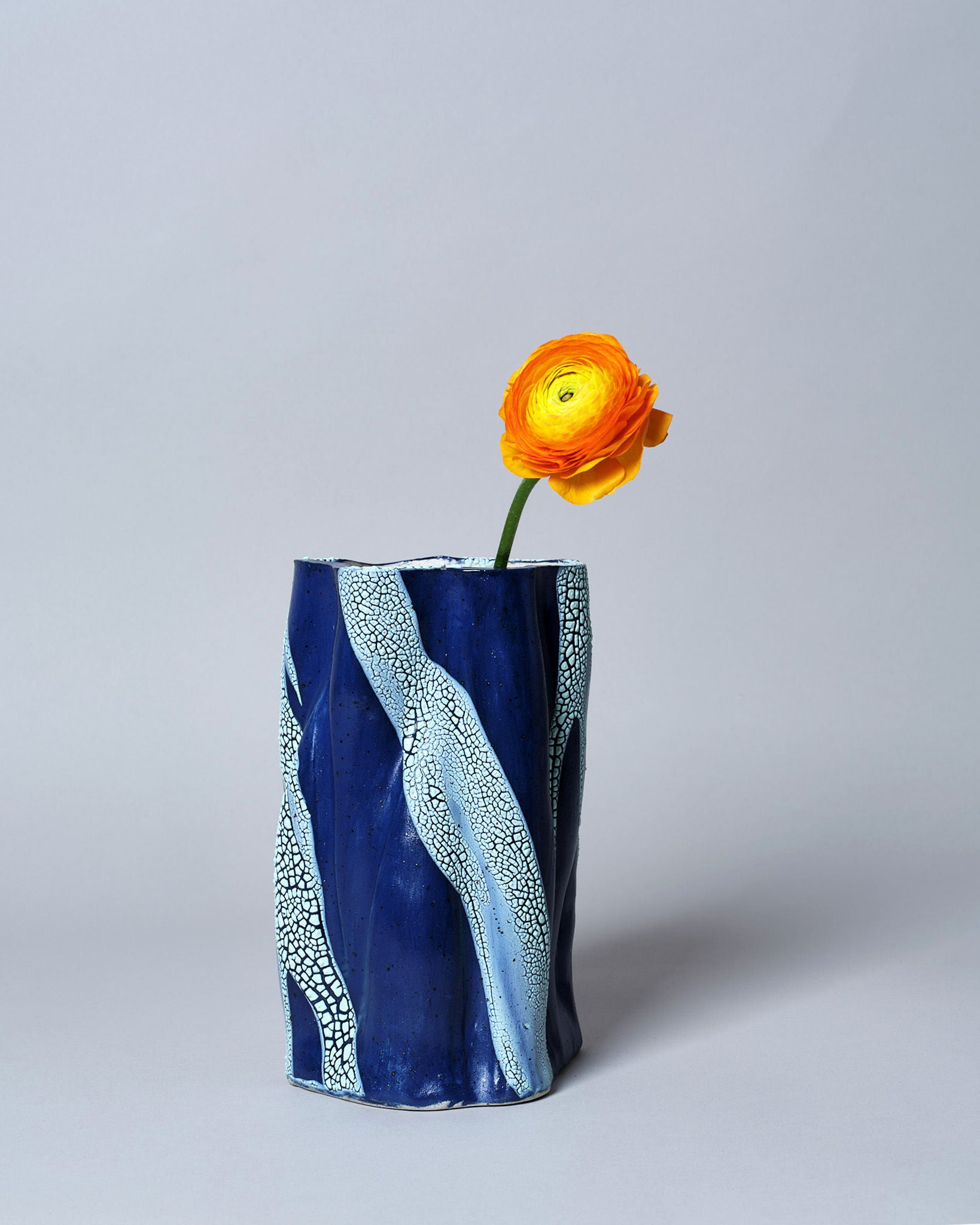 A vibrant orange flower in Astrid Öhman's Swirly Vase Blue and Light Blue, set against a light gray background.