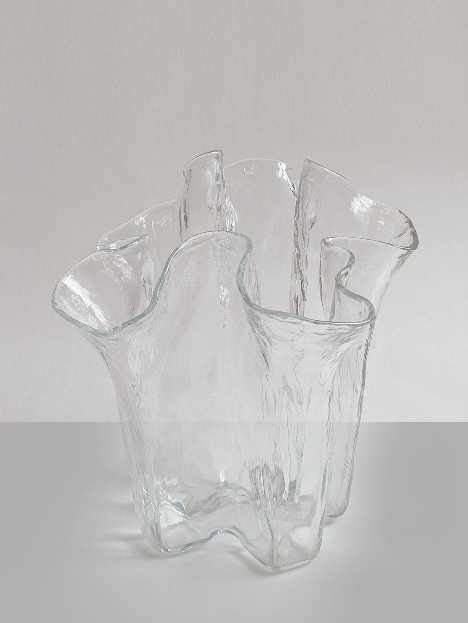 Part of the Eva Collection, the Glass Vase by Pertti Kallioinen for RELIC LONDON features abstract, wavy edges resembling a flowing sculptural form. It stands elegantly on a smooth surface against a neutral background.