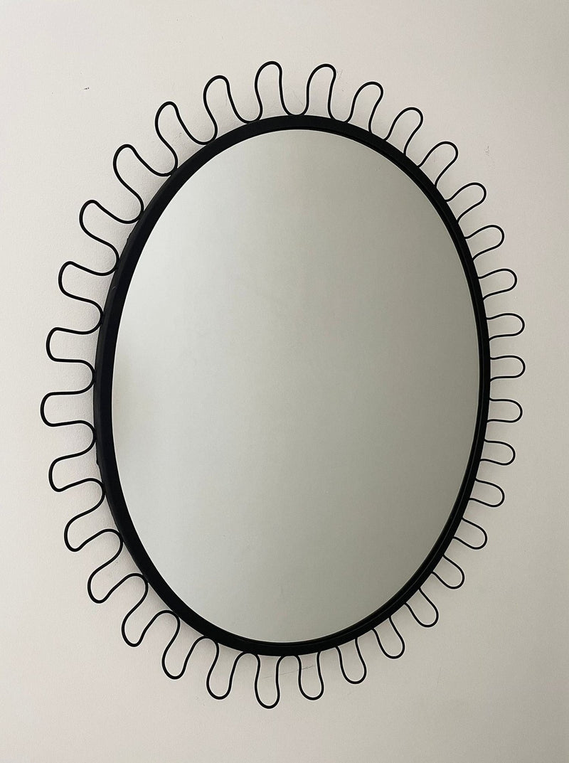 Oval mirror with decorative black metal sunburst frame design