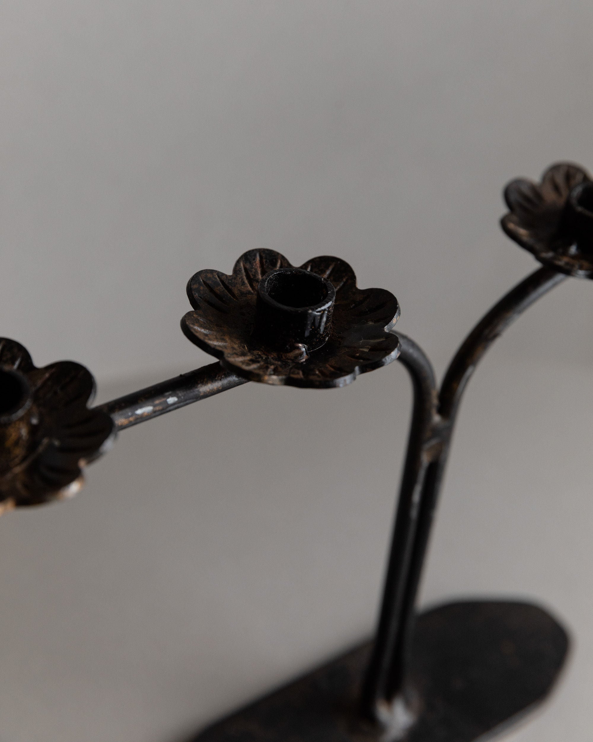 This Iron Candleholder from Bottega Jacobs showcases three flower-shaped holders on curved stems, embodying 1960s Italian design. Its textured, slightly worn surface adds character as a perfect table decoration against a neutral background.