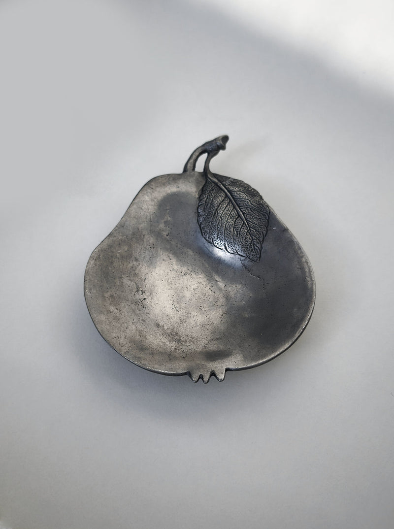 The Pear Vide-poches by Les Objoies is a pear-shaped decorative dish with a metallic brass finish, an attached stem, and a detailed leaf, shown on a plain light background.