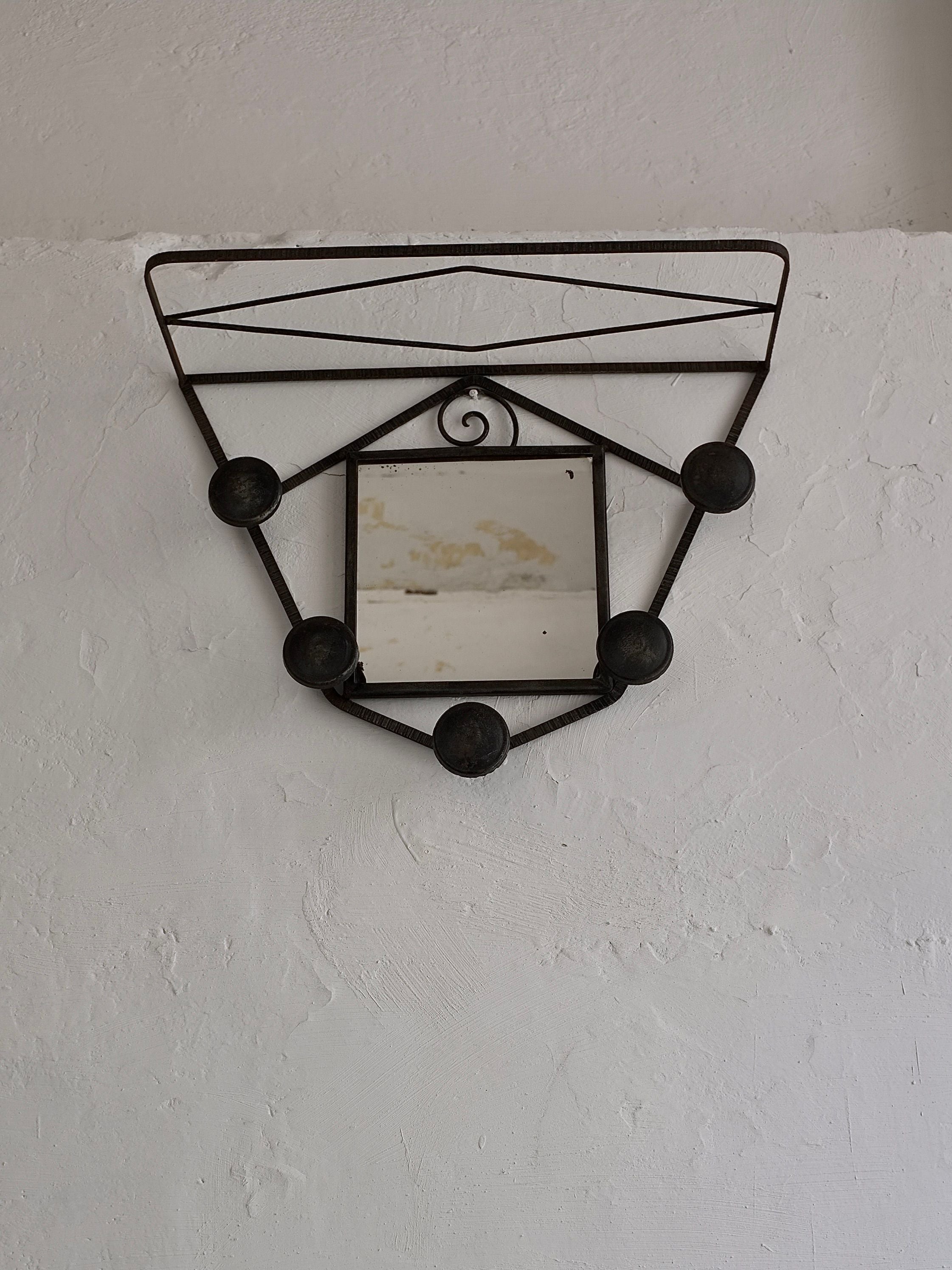 A small, square mirror from the 1930s, featured in the Art Deco Wrought Iron Wall Mirror Coat Rack by Veter Vintage, is framed by a decorative black iron frame against a textured white wall. The French-manufactured ironwork showcases geometric shapes and circular elements, creating a visually intricate and artistic appearance.