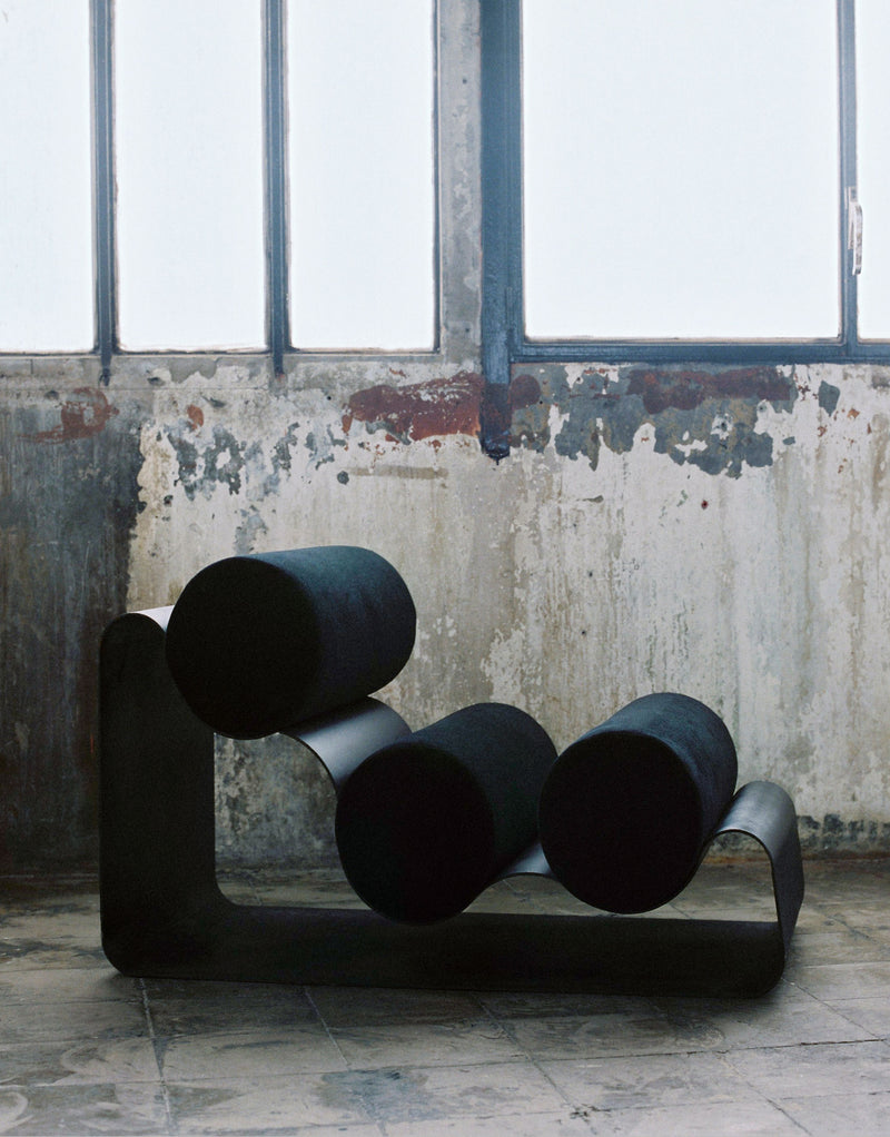 Black sculptural aluminum chair with cylindrical cushions in industrial setting