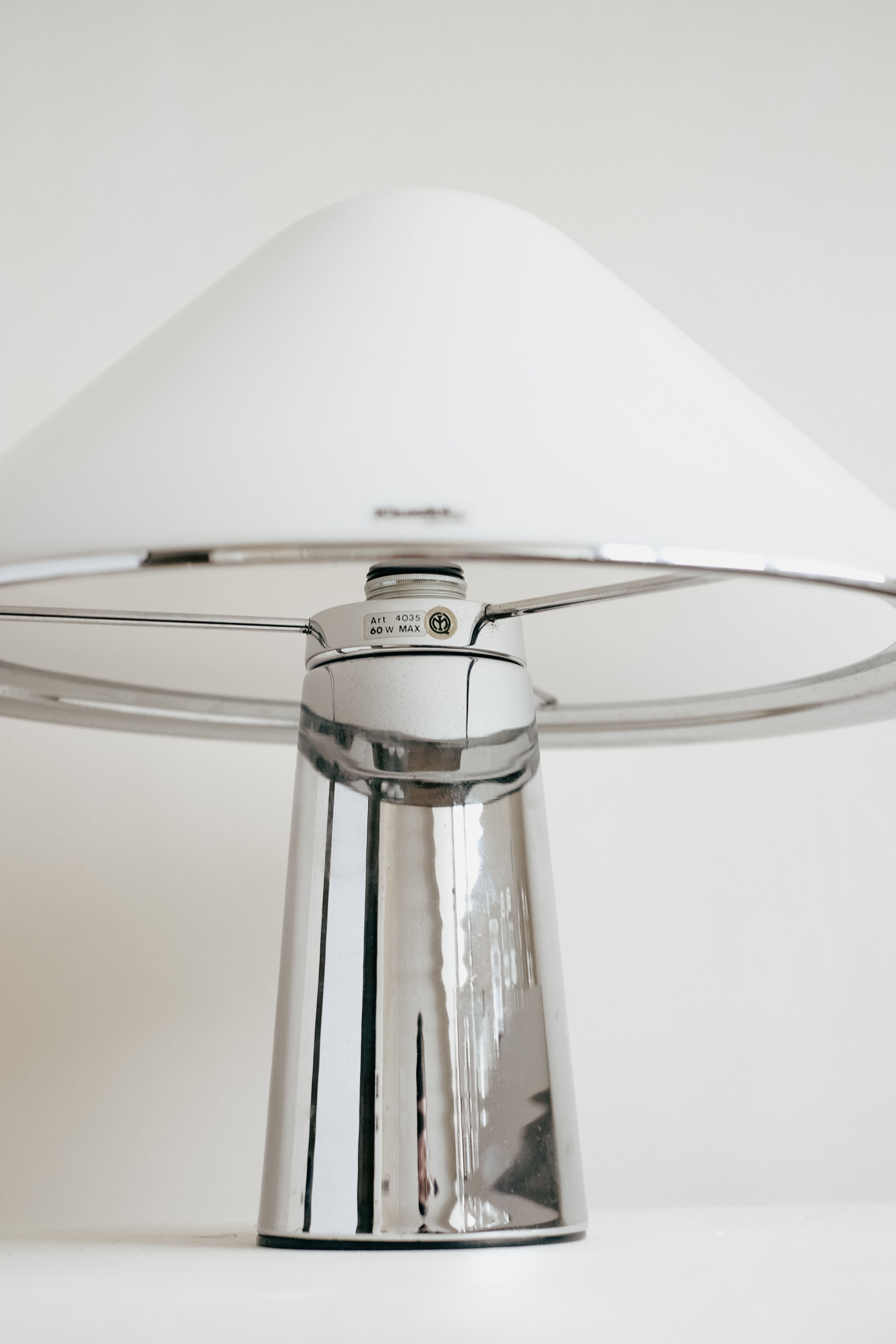 The Harvey Guzzini Elpis Table Lamp by septembre studios features a sleek chrome base and a wide, white dome-shaped shade, presented against a simple, light background.