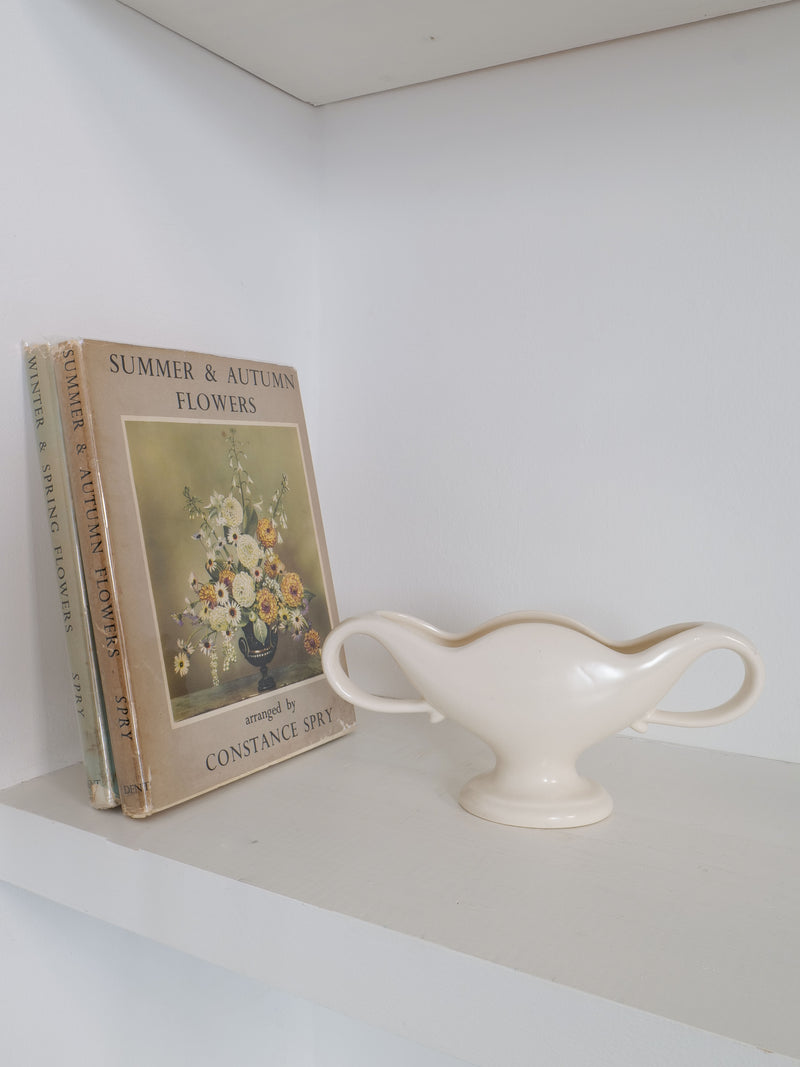 A vintage book titled "Summer & Autumn Flowers" by William J Marriner is placed upright on a white shelf. Next to it, there is a cream-colored, two-handled Mini Mantle Vase 1930s from the brand Collection apart. The book features an illustration of a bouquet of flowers on its cover against the plain white background.