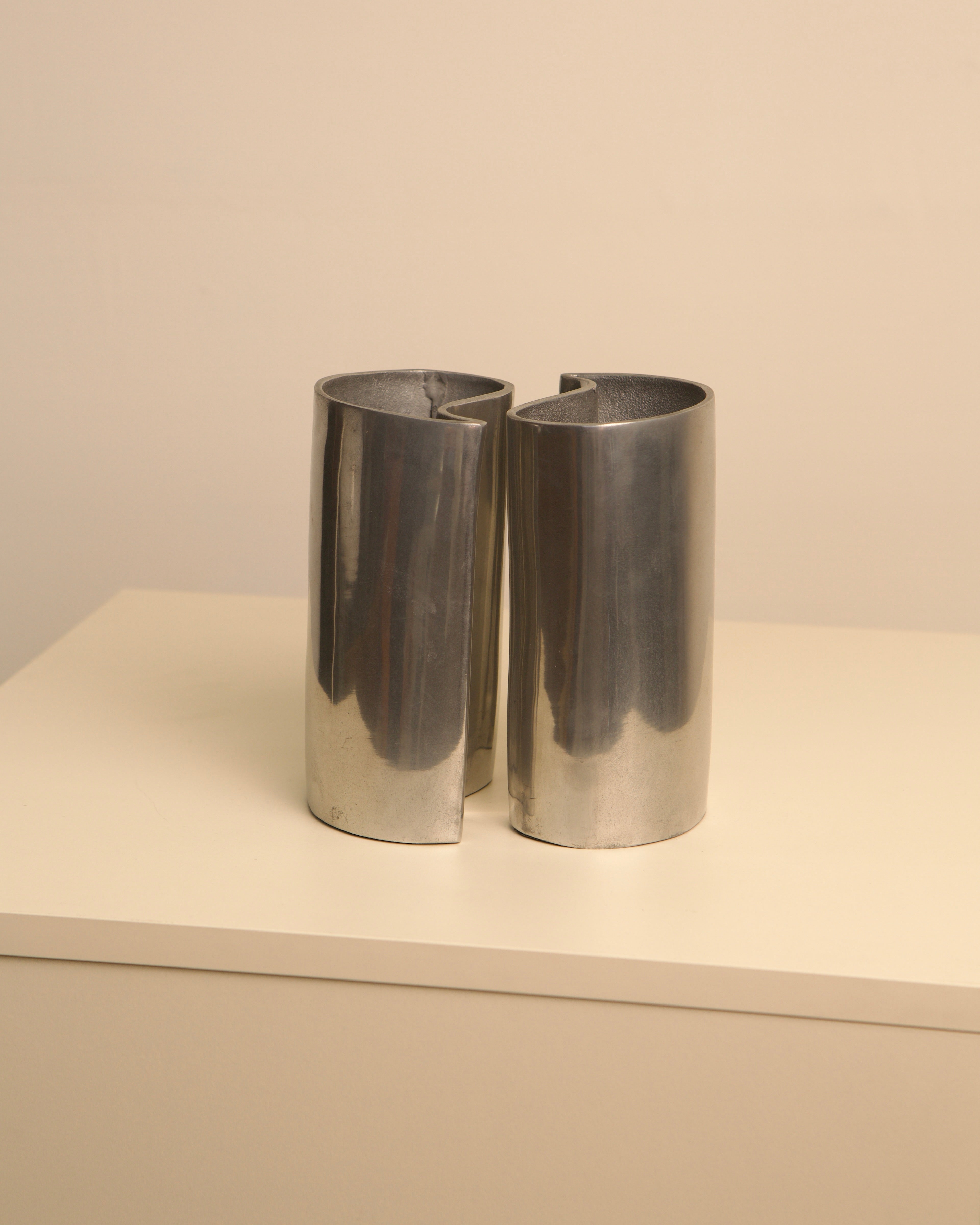 Two polished aluminum cylindrical vases interlocking in yin yang formation