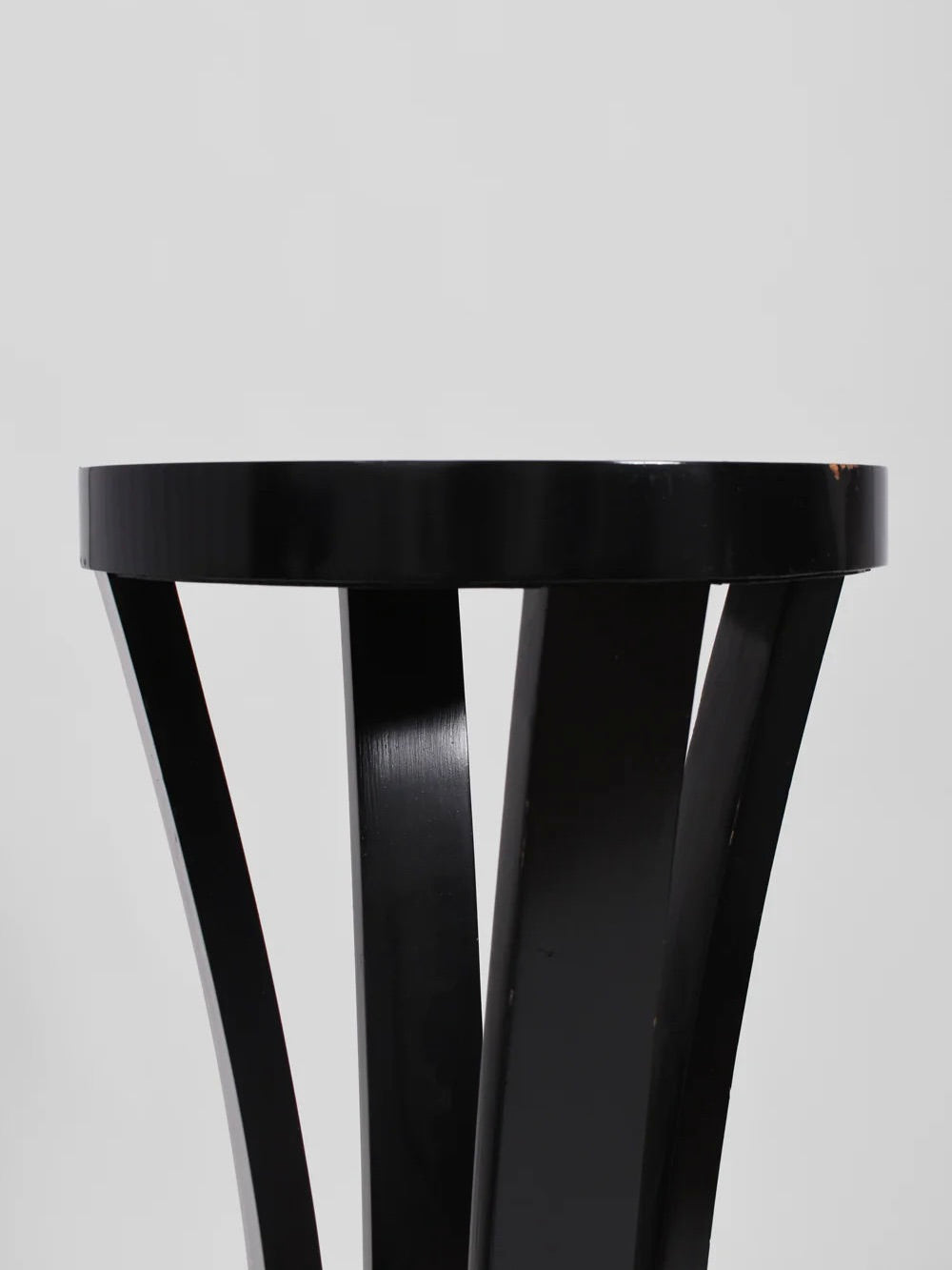 A close-up of the Pair of Black Wooden Pedestal stools by Barracuda Interiors, 1960s, featuring round tops and four slanted legs, shown against a plain light gray background.