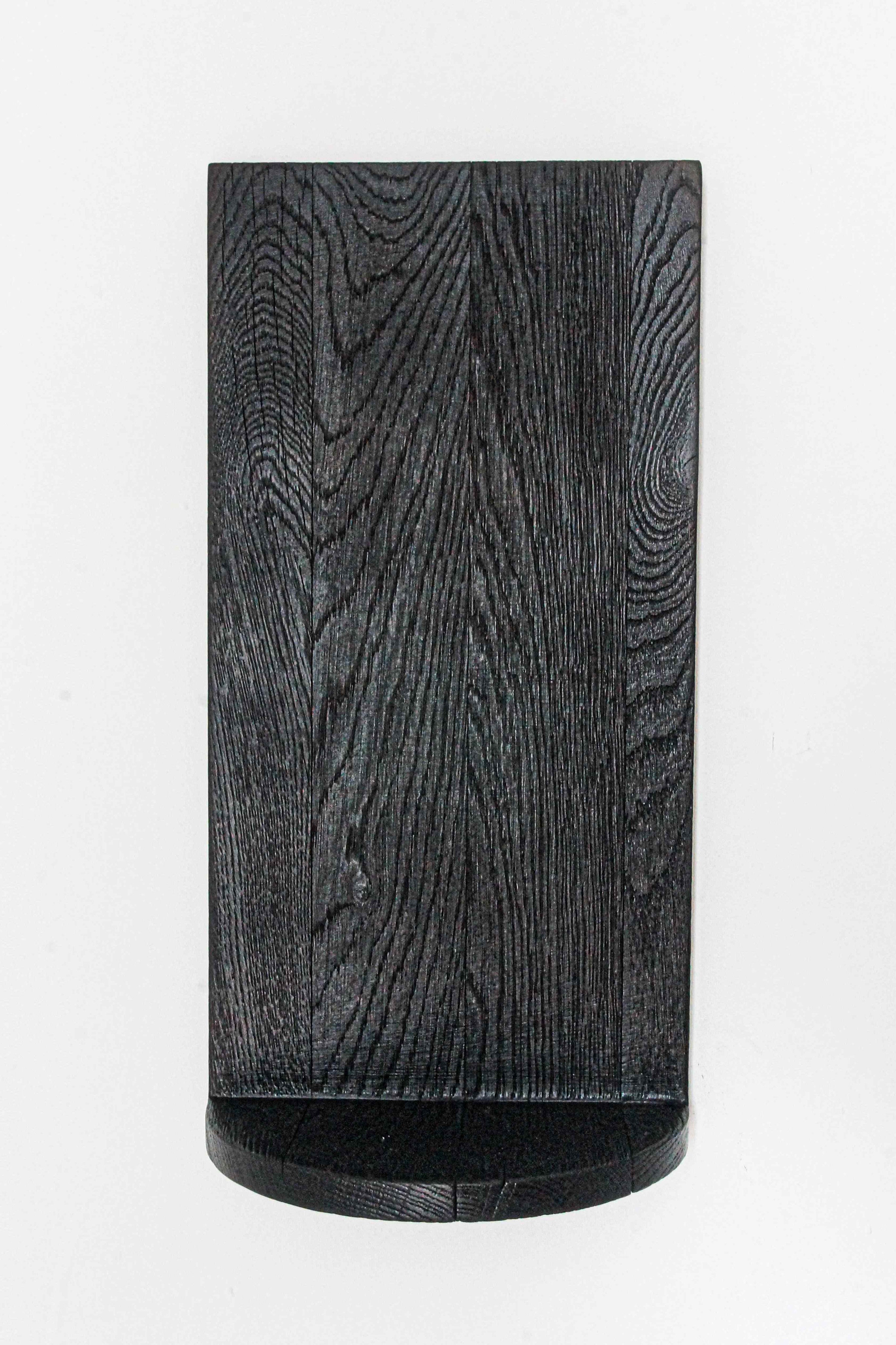 The Megaron - Minimalist Shelf in Wood (Small) by COSEINCORSO features a black solid oak design with a curved bottom edge and visible wood grain, mounted against a white background for a sculptural, handcrafted look.