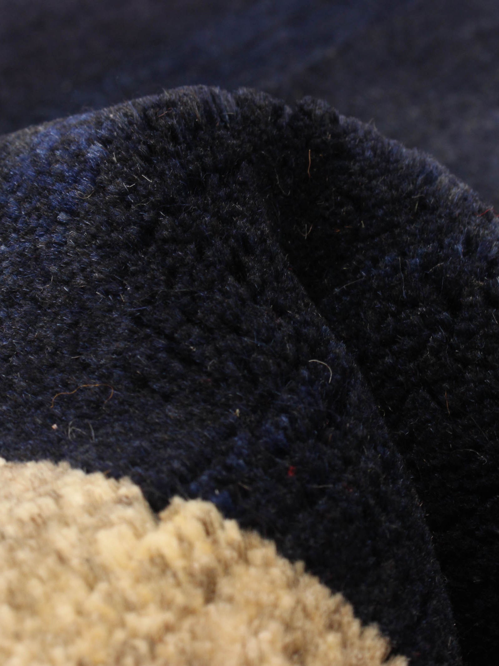 Close-up of a Gabbeh Rug in Midnight by catalog:three, featuring a soft, fuzzy texture with dark-colored dense fibers and a beige section, size 93 x 183 cm. The slightly coarse surface accentuates the unique color variations between dark and light areas.