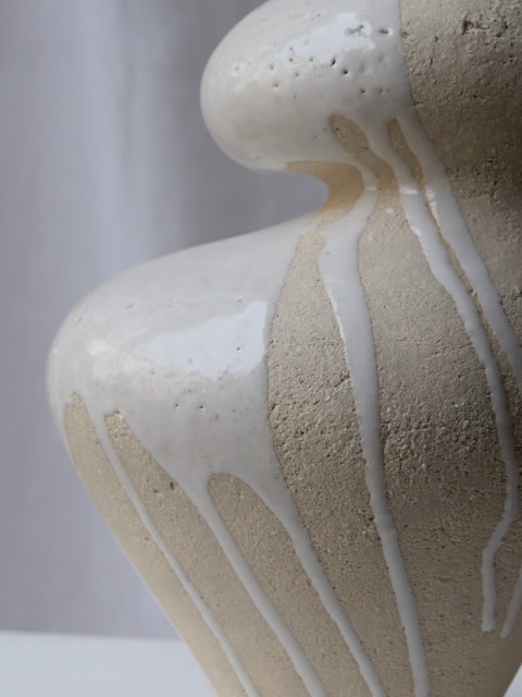 Close-up of Lucia Mondadori's Lilith White Drip vase, featuring a beige stoneware base with a glossy white glaze dripping down its sculptural curves, set against a plain light background.