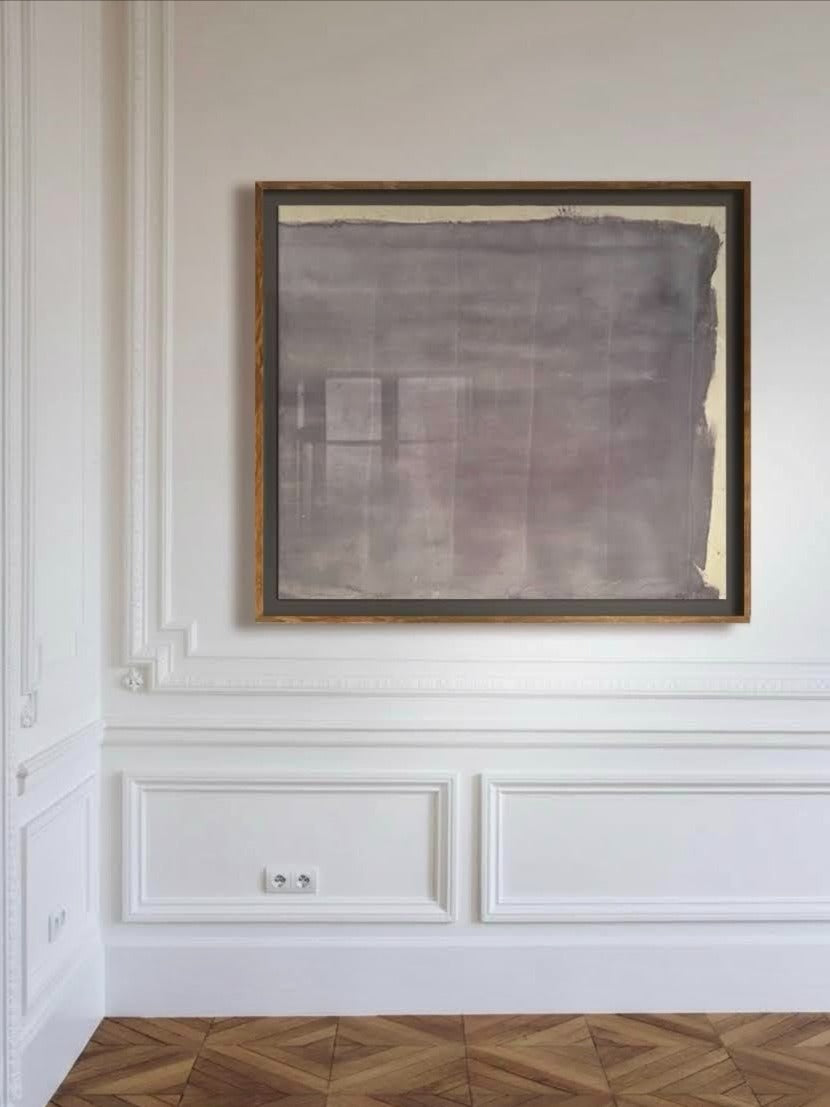 A large “Gray Mauve” pigments and ink on raw canvas by Médecine hangs in a simple wooden frame on a white wall with ornate molding above a herringbone wood floor, featuring muted gray and brown tones in an abstract style.