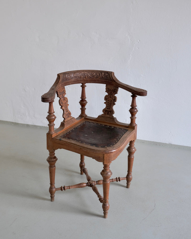 Antique carved wooden corner chair with black leather seat