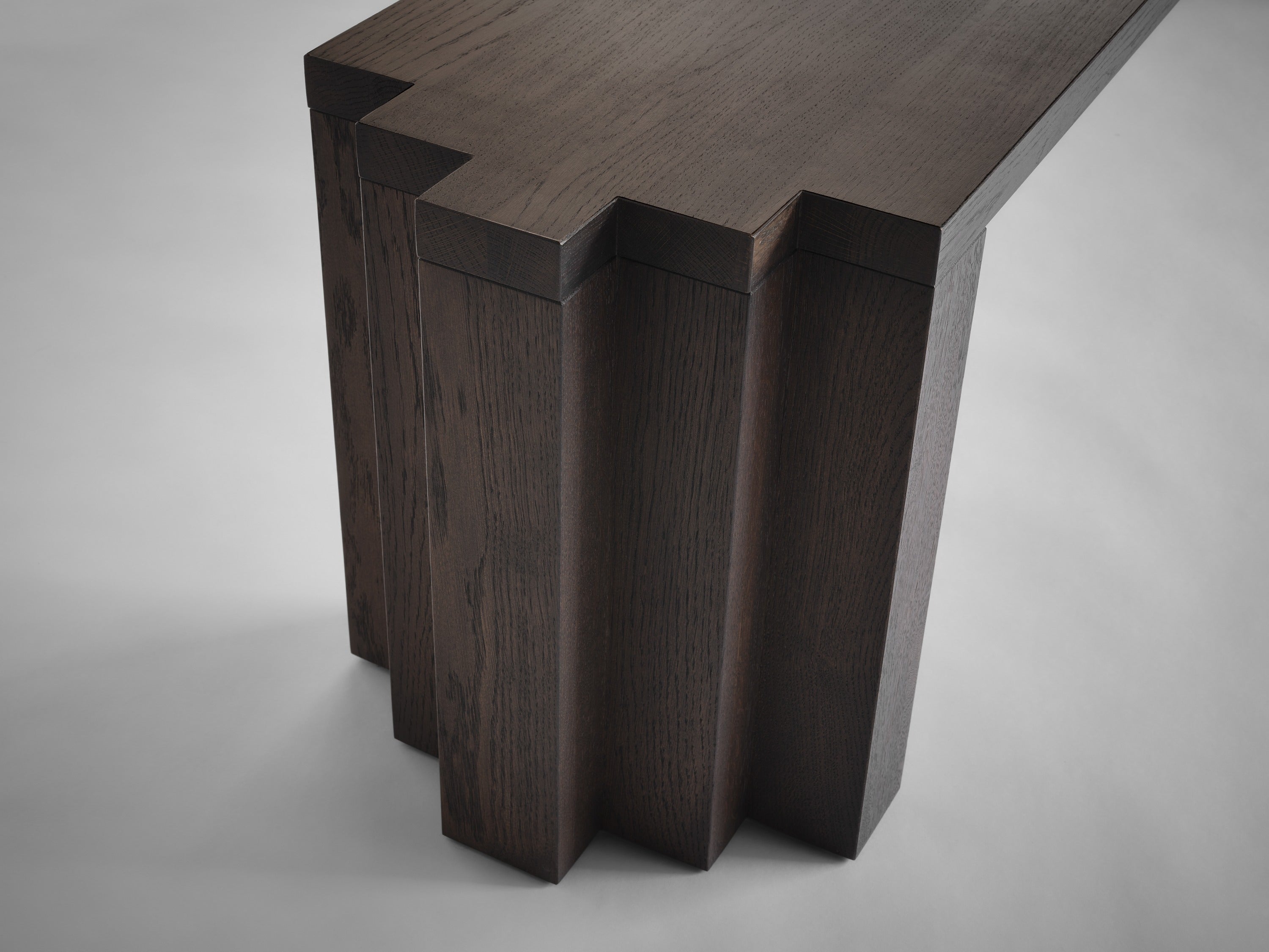 The Cadence Bench by Mokko features solid European oak with a dark finish, geometric base and staggered, stepped edges. Visible wood grain highlights its craftsmanship, all set against a light background.