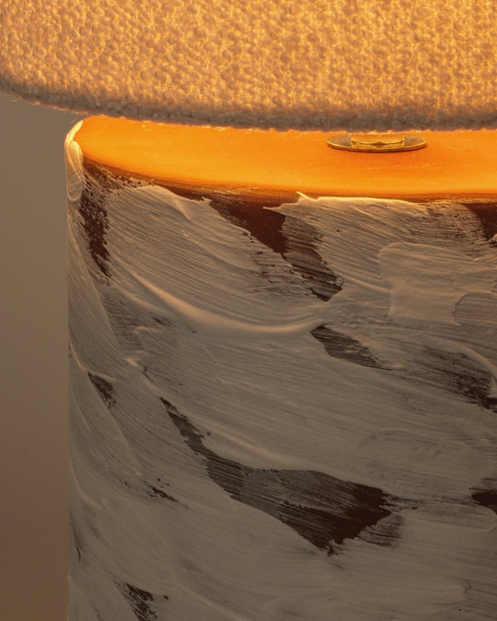 A close-up of the Katia Langeard White Wind Table Lamp in ceramic, featuring a textured white and brown painted base and a light-colored shade that creates a warm bedside ambiance.