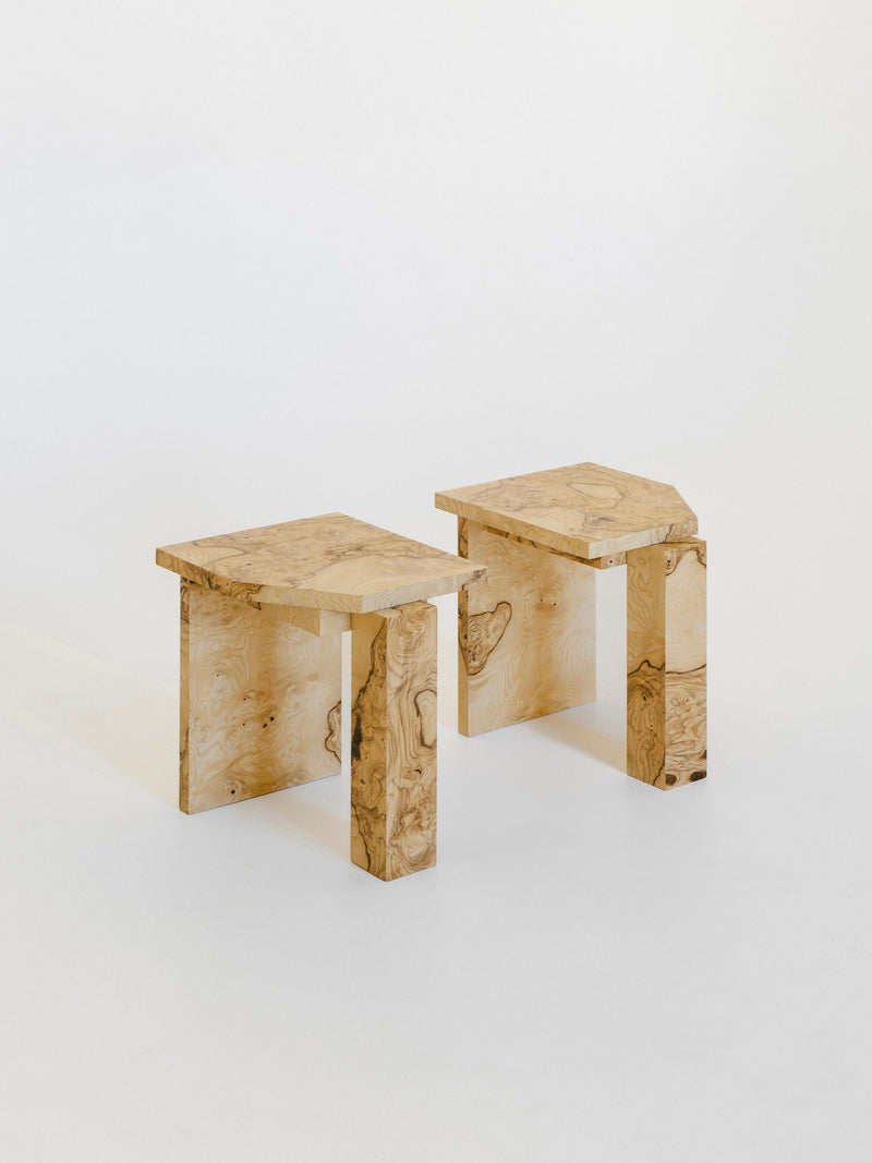 The SSS01W Stool by sashaxsasha features angular, geometric shapes and visible wood grain. These modern wooden stools blend style and function, shown here on a plain white background.