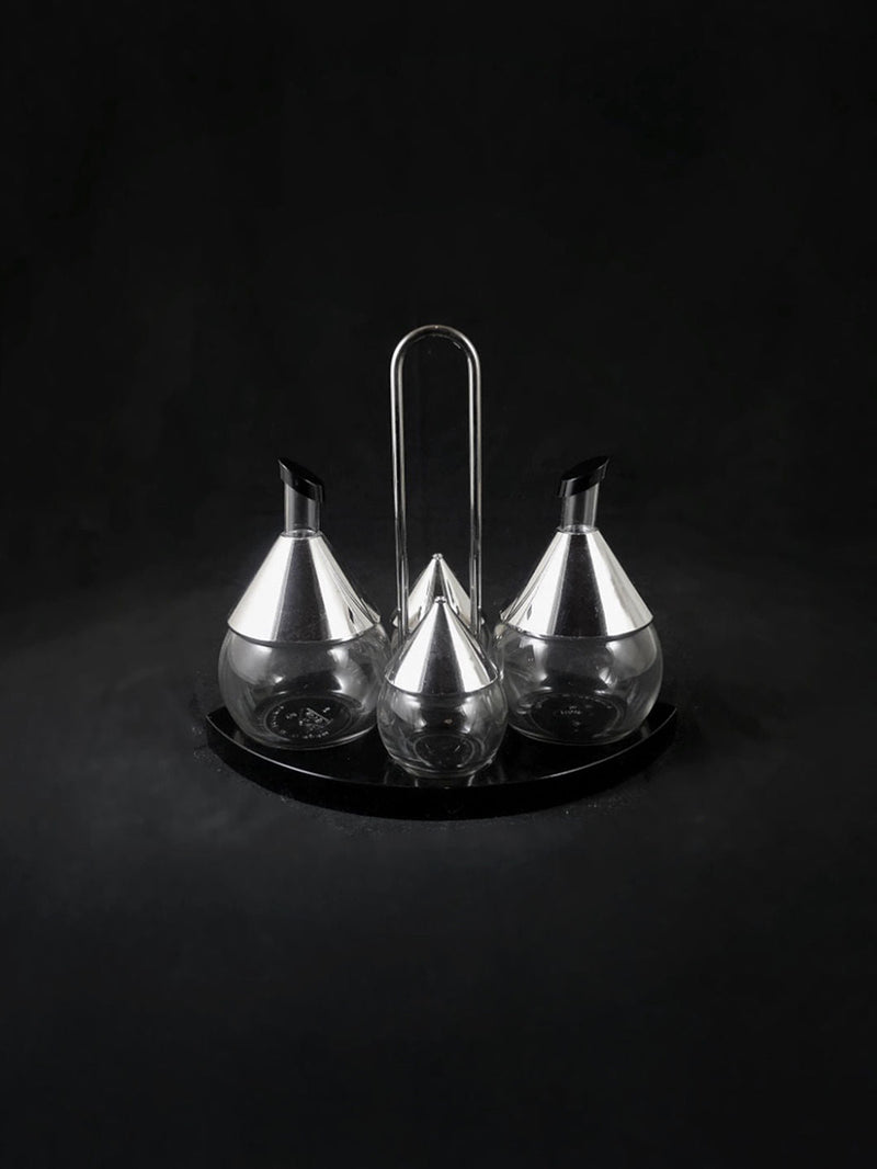 The Dodo Vintage Italian Chrome Menage 1980s set features three glass and metal condiment dispensers on a round tray with central handle, shown against a black background. Made in Italy.