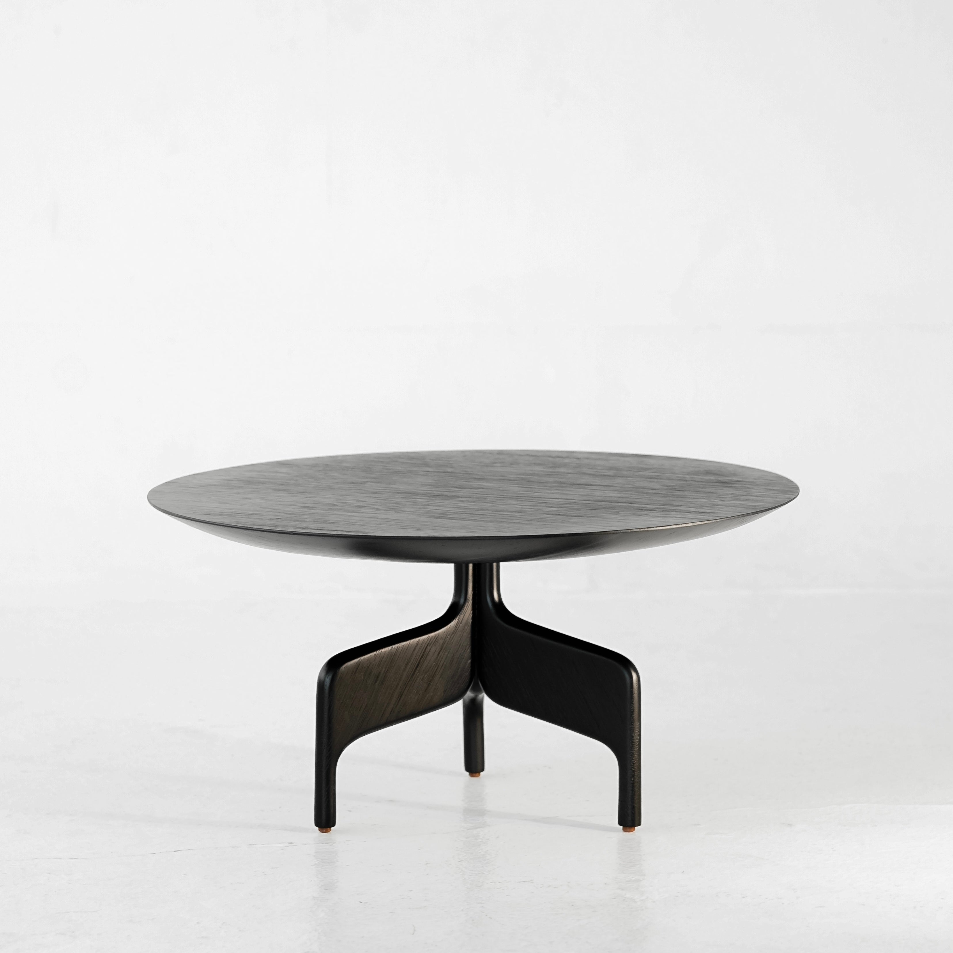 The "Alaia" Table by Luciano Costa Estúdio is a modern, round black coffee table from the Nômade collection with a smooth top and three curved solid jequitibá legs, shown against a plain white background.