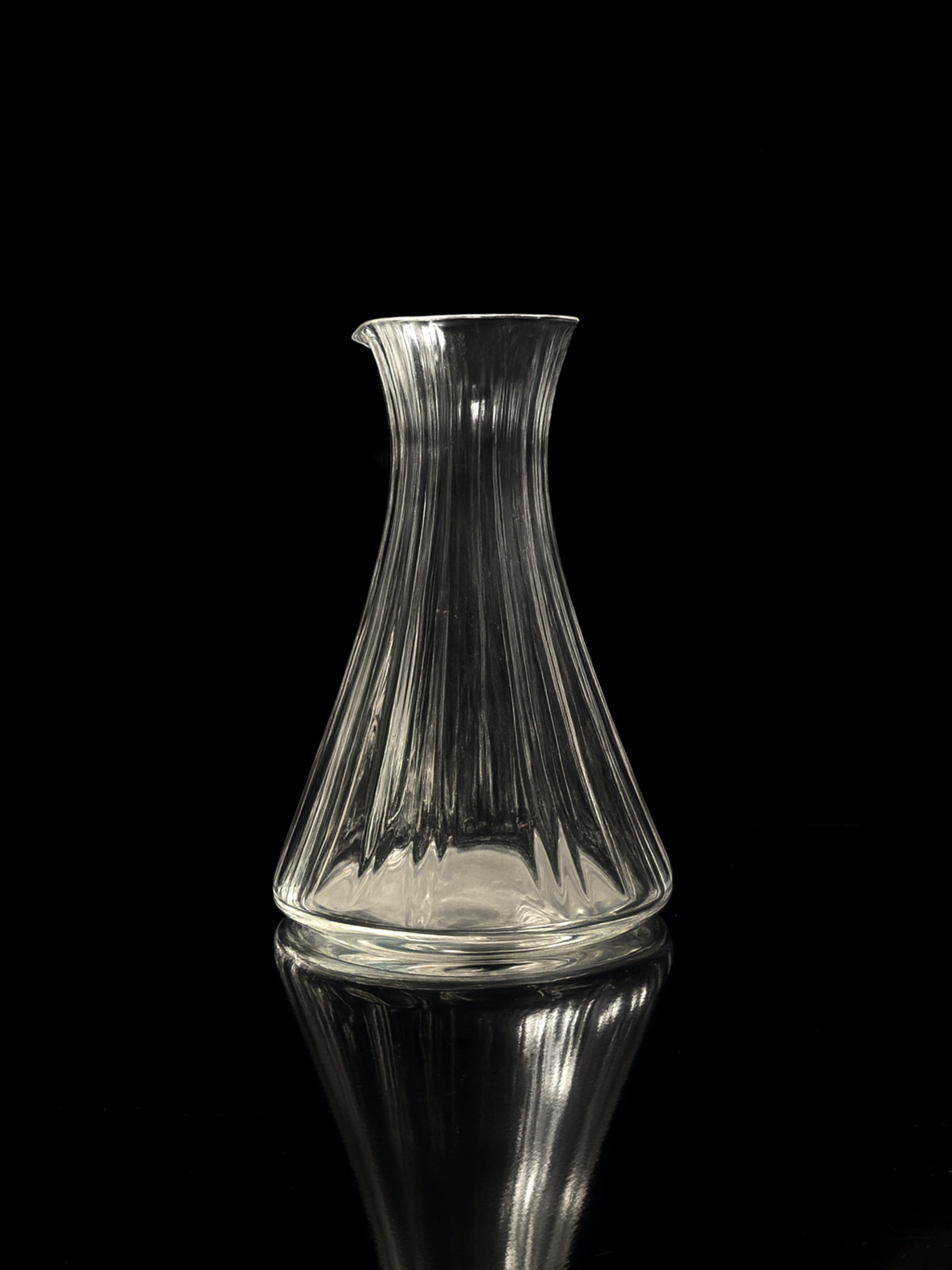 The Dodo Vintage Italian champagne and wine crystal carafe features hand-cut vertical ridges and rests on a reflective black surface, creating a subtle mirrored effect against the dark background.