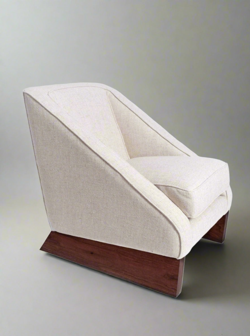 The Arrábida Armchair by Barracuda Interiors features modern beige upholstery, angled sides, and a wooden base, shown against a plain light background.