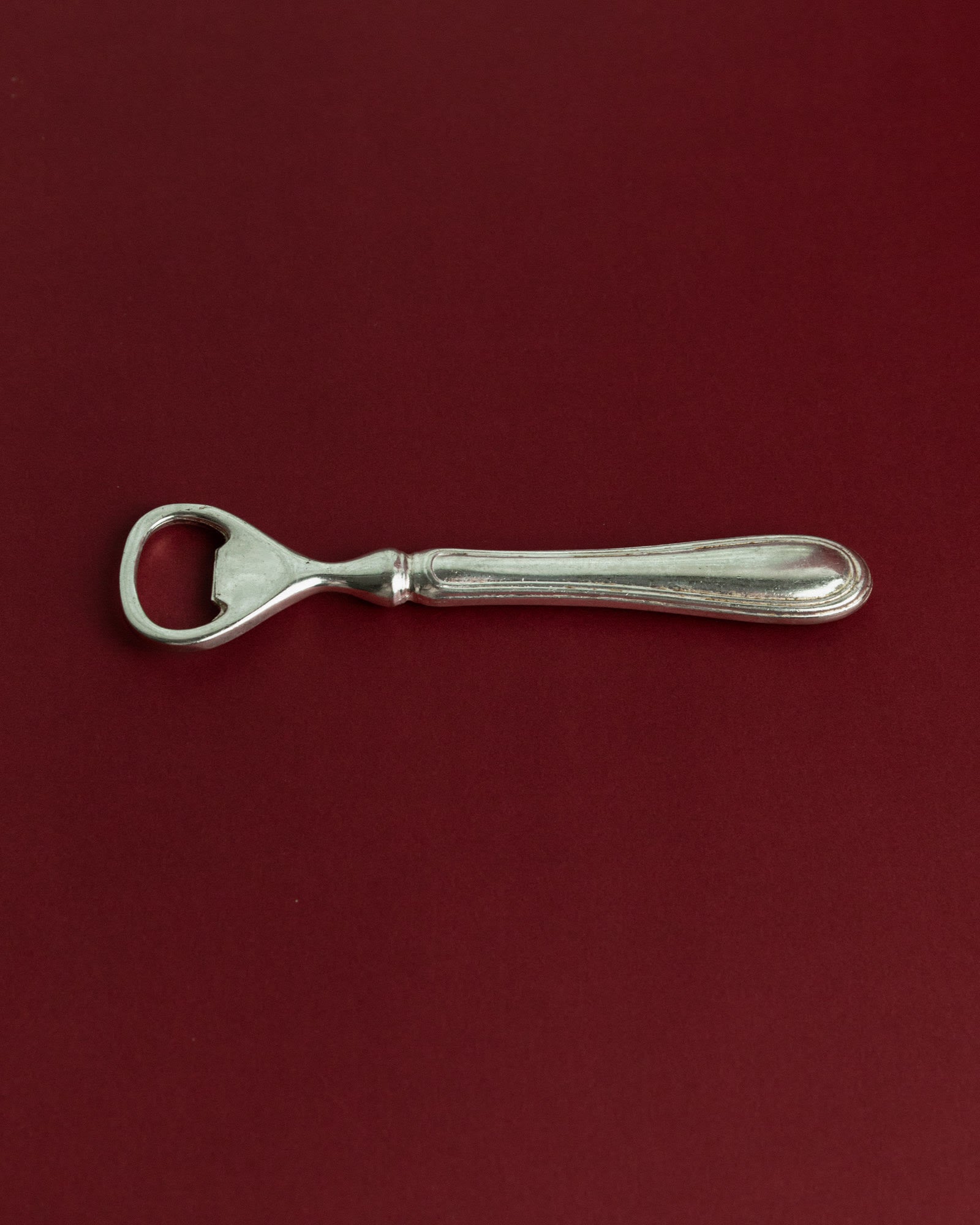 Vintage 1960s Silver Plated Bottle Opener, Classic Minimal Design, Retro Bar Accessory — top view on burgundy background