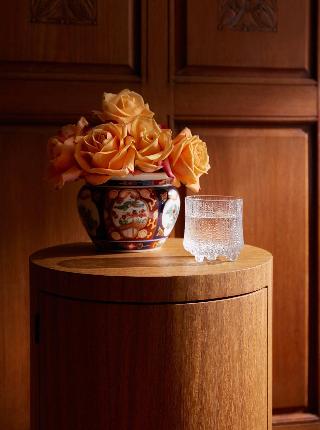 Pair of Constant Nightstand in Oiled Iroko — side angle with floral arrangement and glass