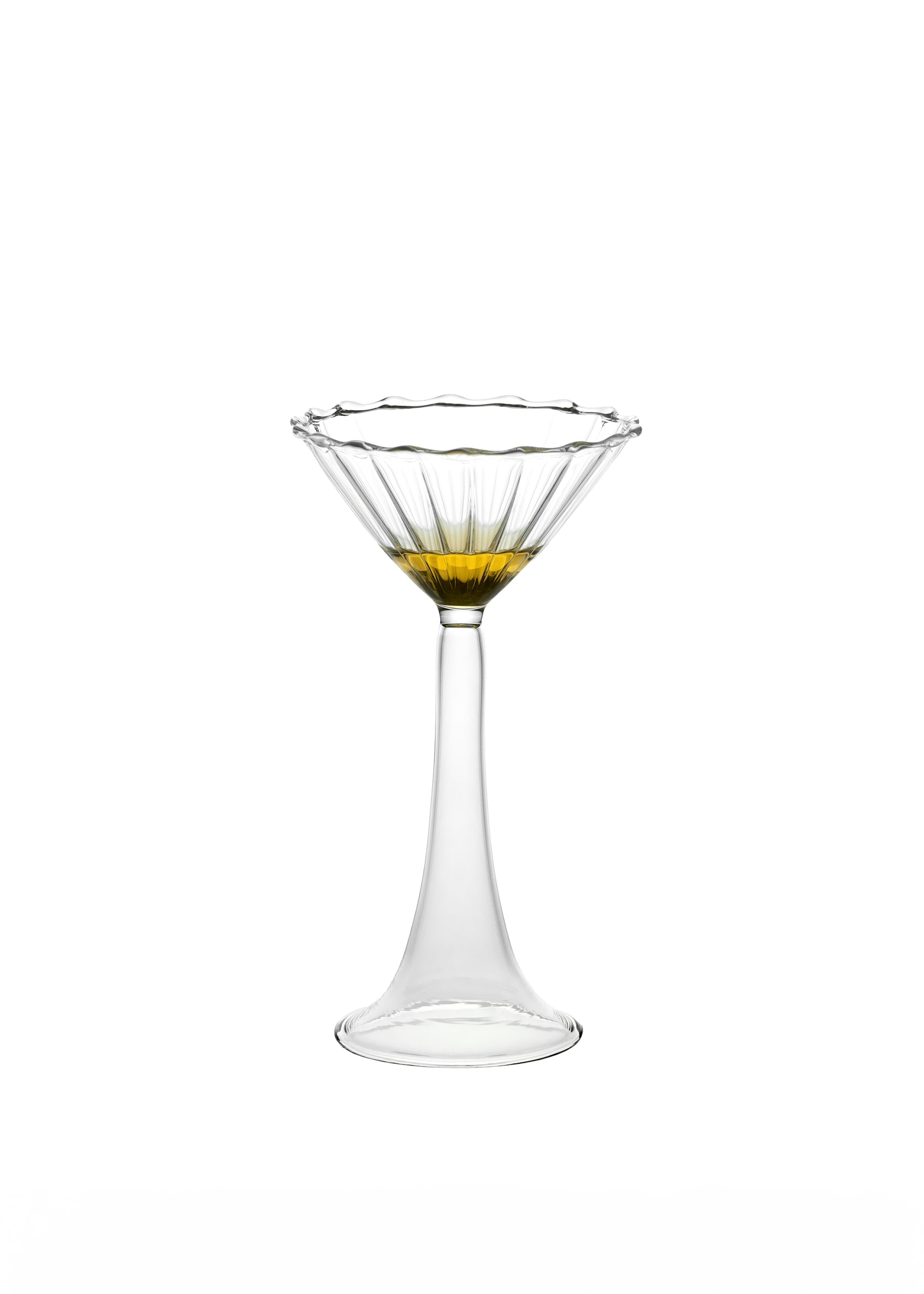 The Campanula — Clear Cocktail Glass by Agustina Bottoni features a wide, fluted bowl handmade in Italy from fine borosilicate glass, holding a splash of yellow liquid against a plain white background.