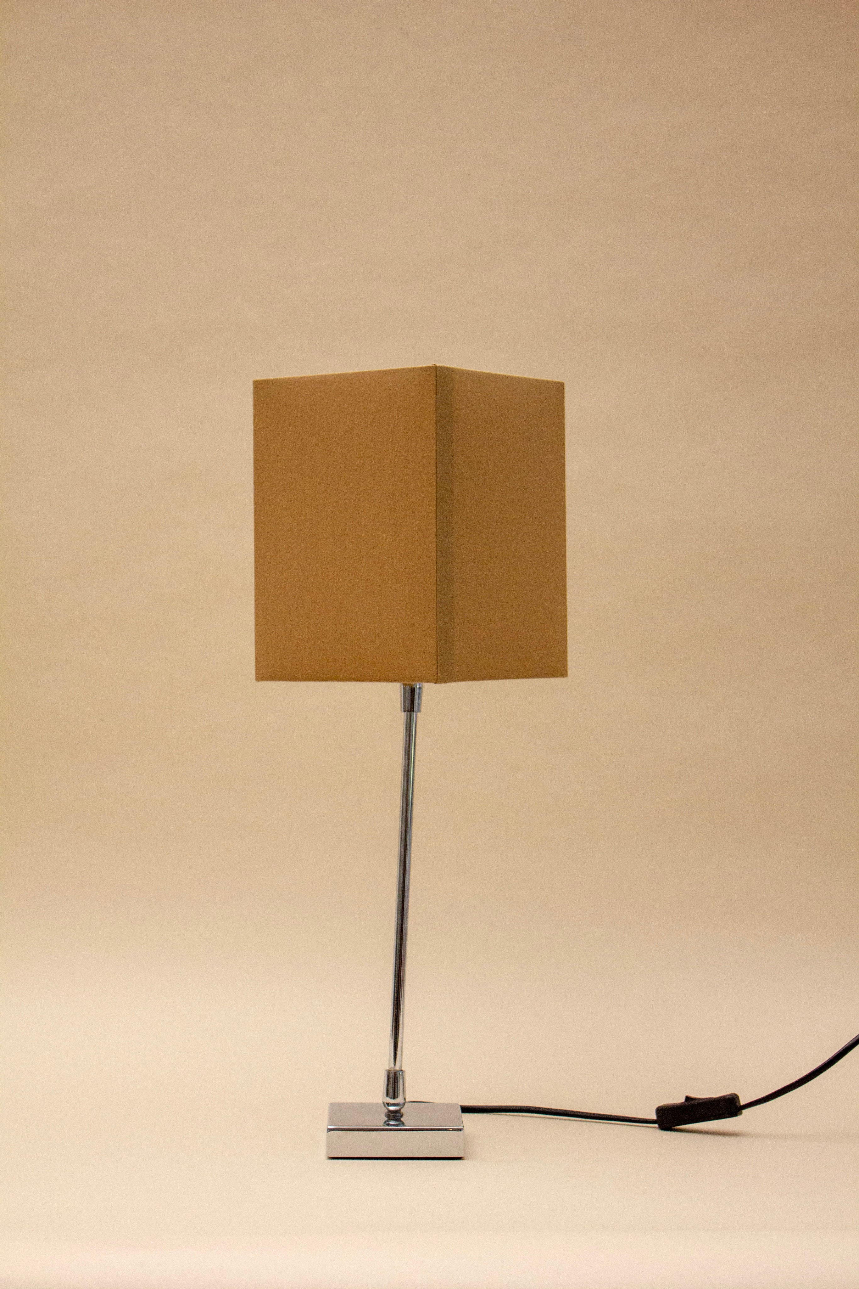 The ZAFRA 2 TABLE LAMP by SÒLER features a rectangular beige shade, slim metal stand, square metallic base, and a black power cord with switch on the right side, all set against a plain background.