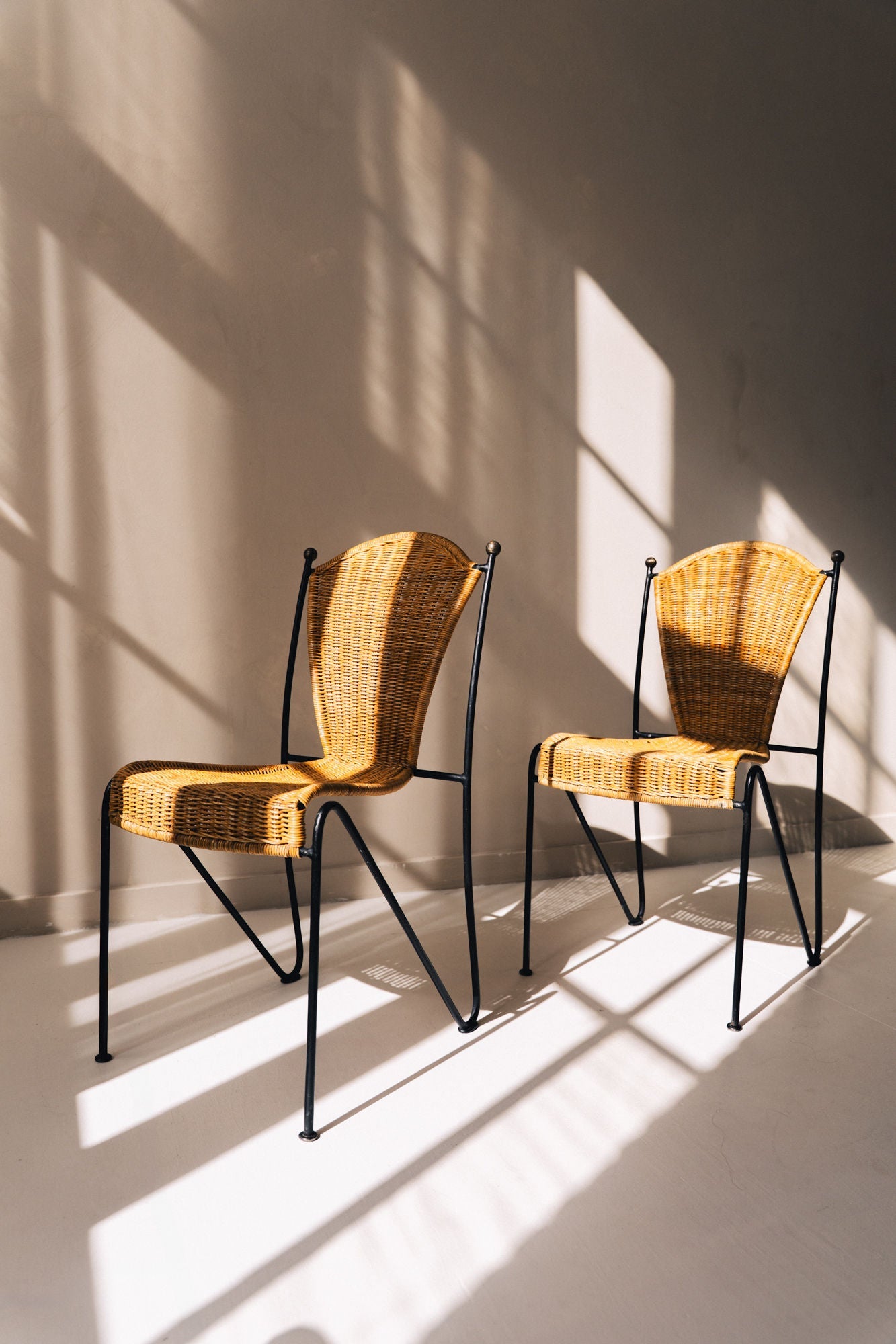 Two Frederic Weinberg wicker chairs with black iron frames in sunlight