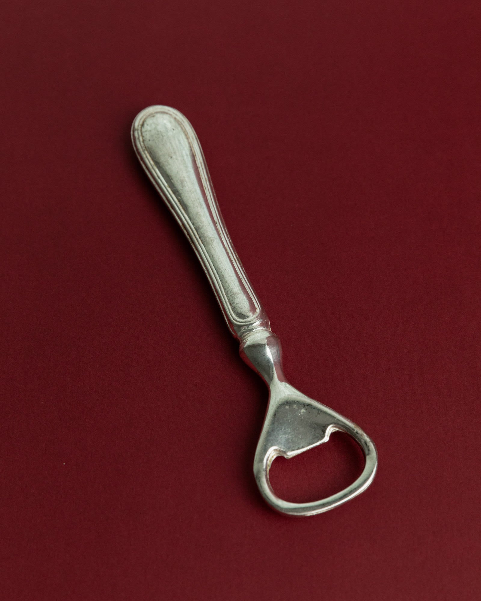 Vintage 1960s Silver Plated Bottle Opener, Classic Minimal Design, Retro Bar Accessory — angled view on burgundy background