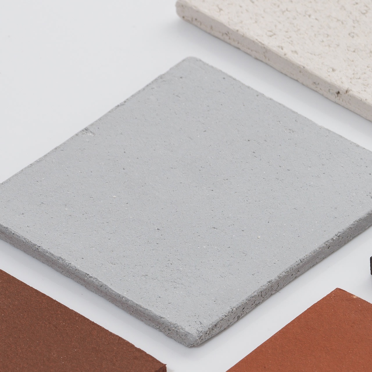 A close-up of four square tiles in various colors and textures, displayed on a white surface—ideal inspiration for styling with the 'Too 60' Ceramic Table Lamp by Katia Langeard.