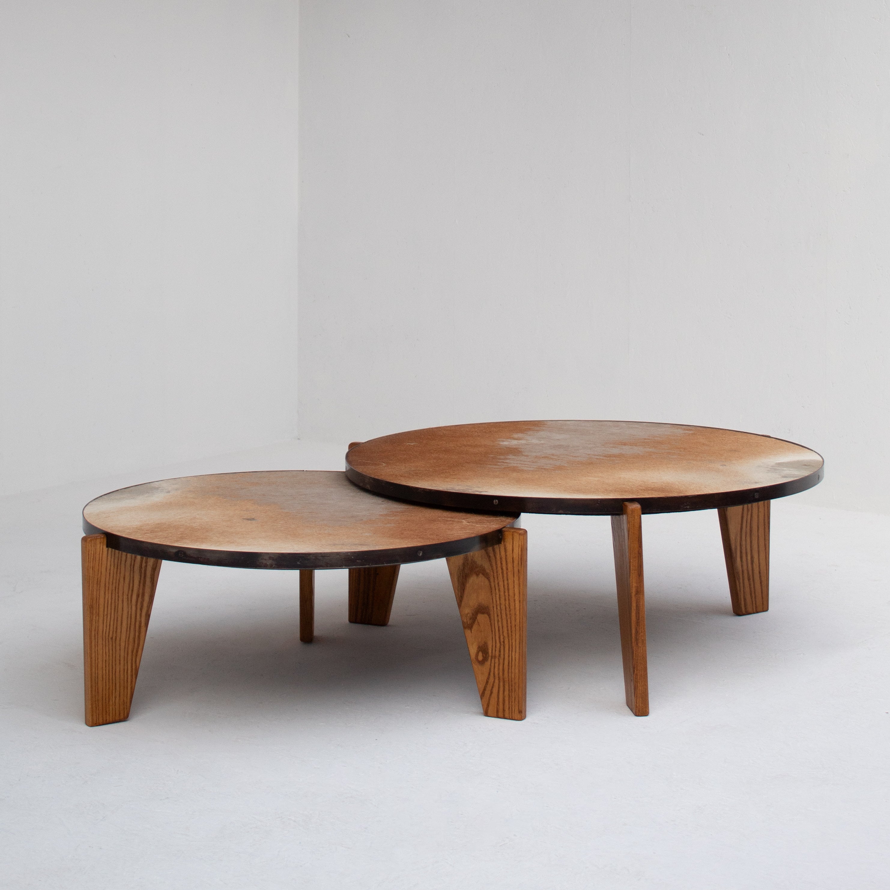 2 Coffee Tables in Wood and Cowhide — side angle showing round tops and wooden legs