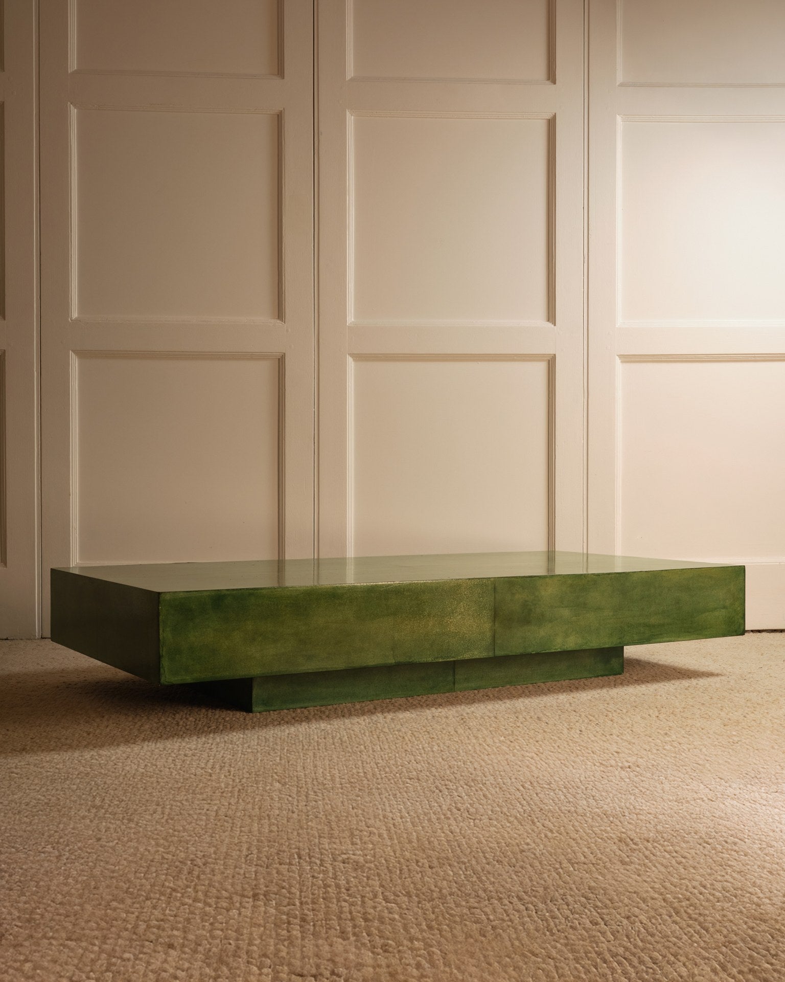 The Green Parchment Table by Galerie Vauvart, a modern rectangular Italian design in glossy green, stands on a textured beige carpet against cream-paneled walls in a softly lit room.
