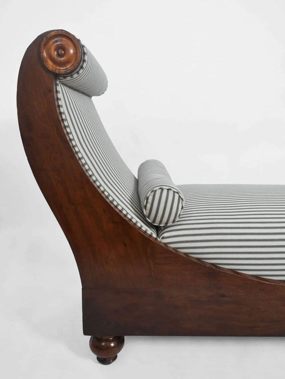 The Neoclassical Daybed, 19th Century by Barracuda Interiors features striped upholstery, a curved backrest, matching bolster pillow, polished finish, and rounded legs for timeless elegance.