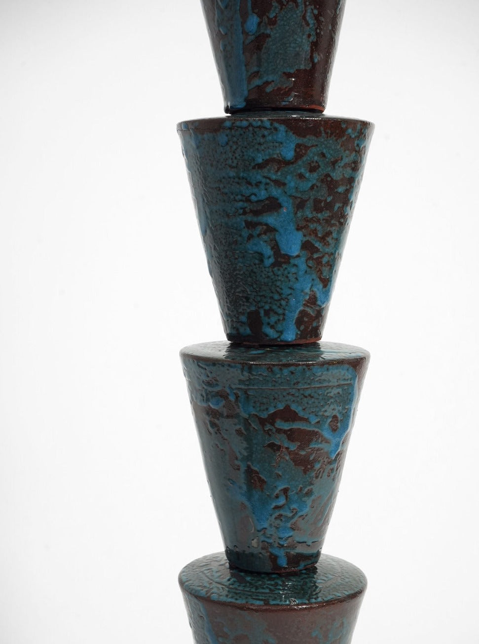 Four blue and brown glazed ceramic cones are stacked vertically in the Barracuda Interiors "Nizwa" Floor Lamp, balancing one atop another against a plain white background.