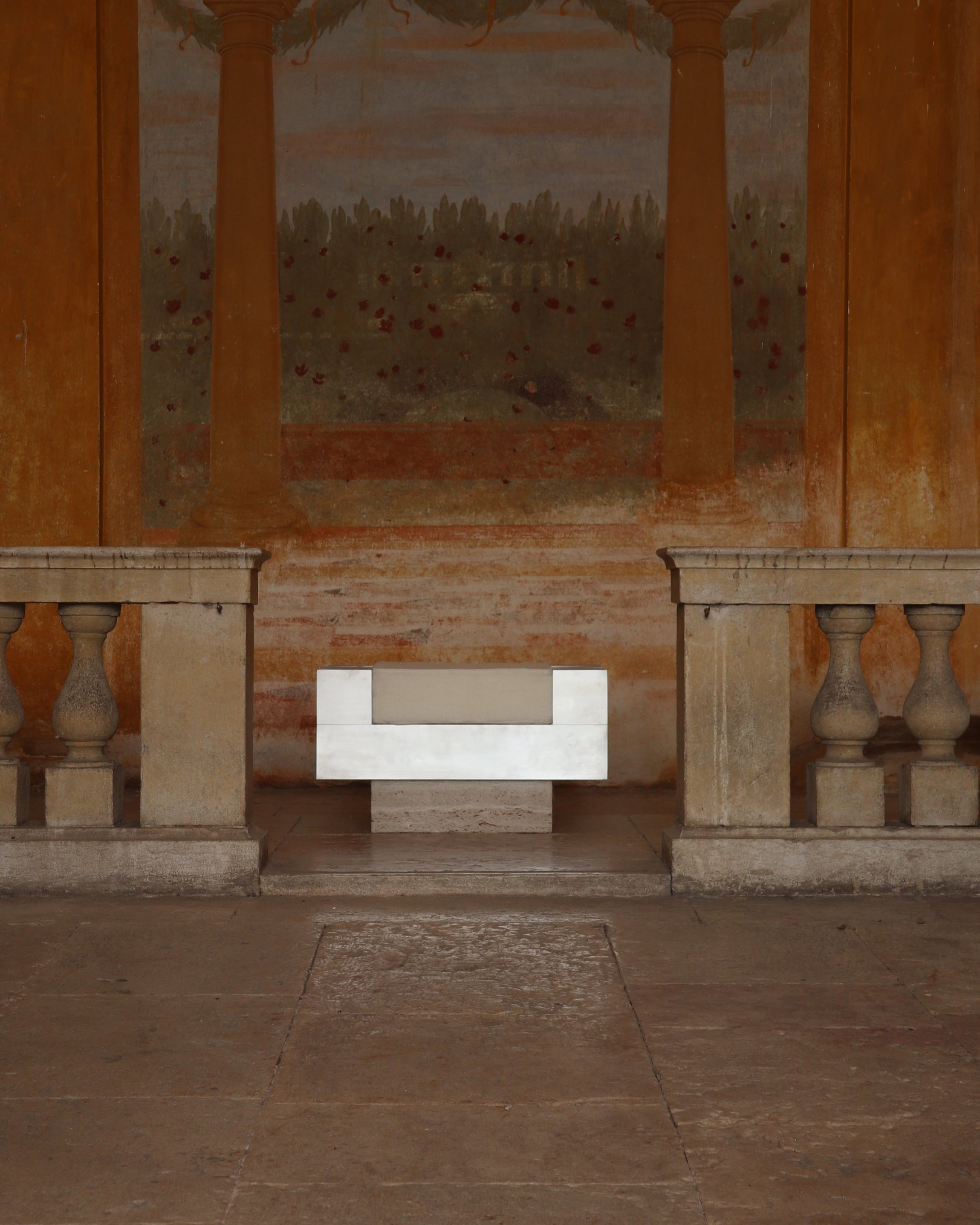 White modern piano ottoman positioned in classical stone colonnade setting