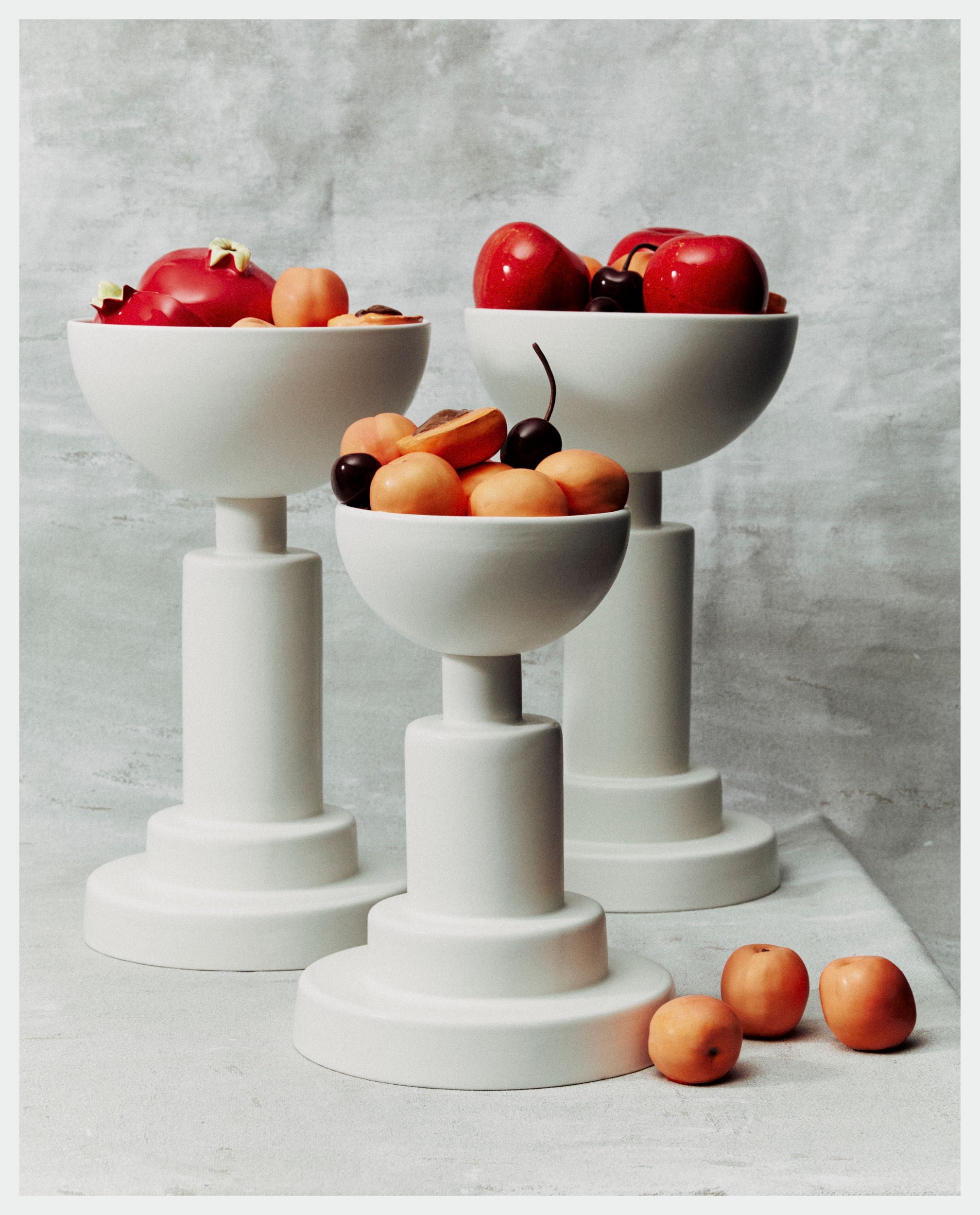 White glazed earthenware fruit bowls on pedestals with apricots and cherries