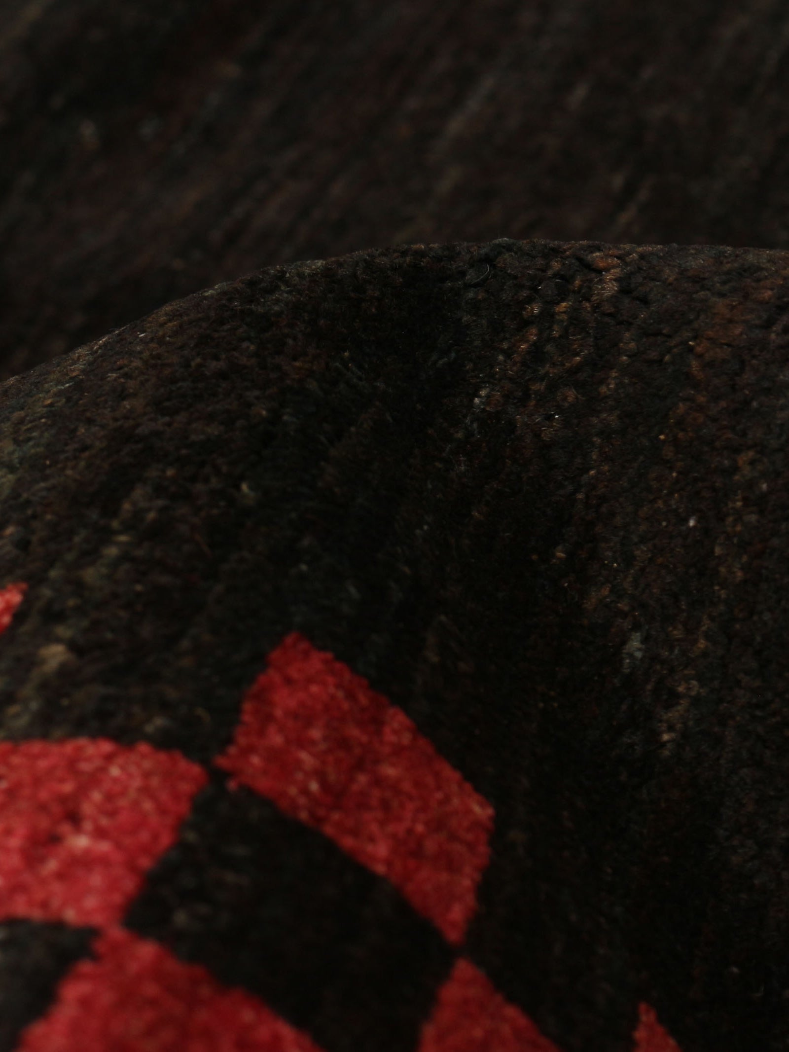 A close-up of a textured dark fabric featuring red and black squares along the lower edge recalls the unique style of a catalog:three Ziegler Rug in Obsidian 247 x 277 cm. The surface appears soft and slightly raised, indicating a thick and cozy material.