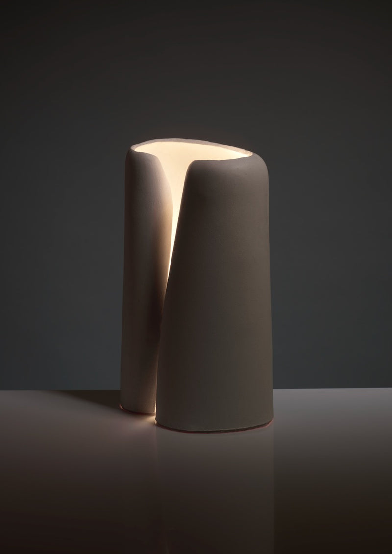 The Snail Table Lamp in Ceramic by Katia Langeard features a smooth matte finish and organic split design that emits soft, warm light from its hollow center—an ideal bedside lamp for dark backgrounds.