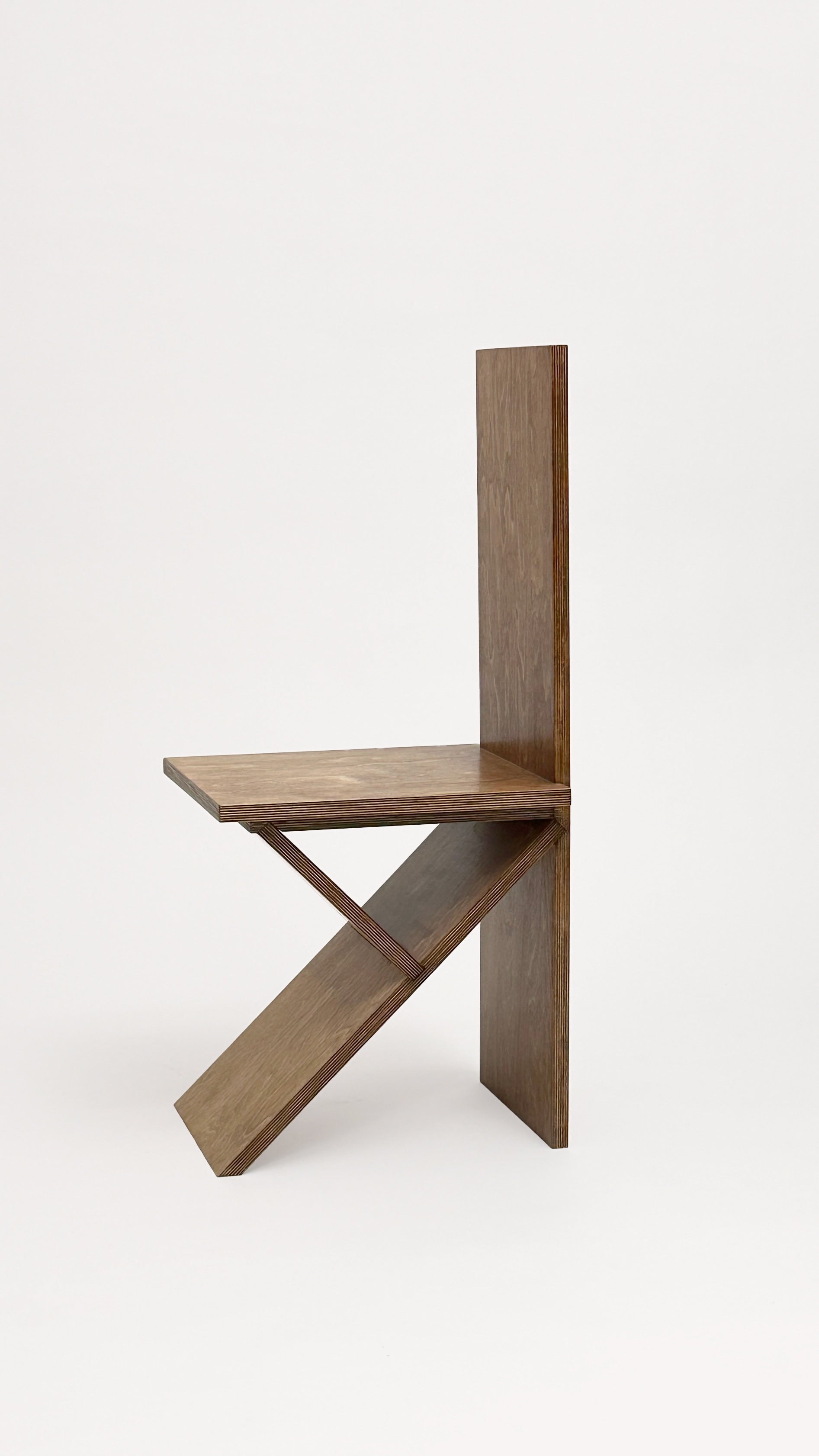 The Flat Pack Chair by Goons from GOONS features geometric lines and minimalist design, with three intersecting wooden panels forming the backrest, seat, and support. Displayed against a plain white background.