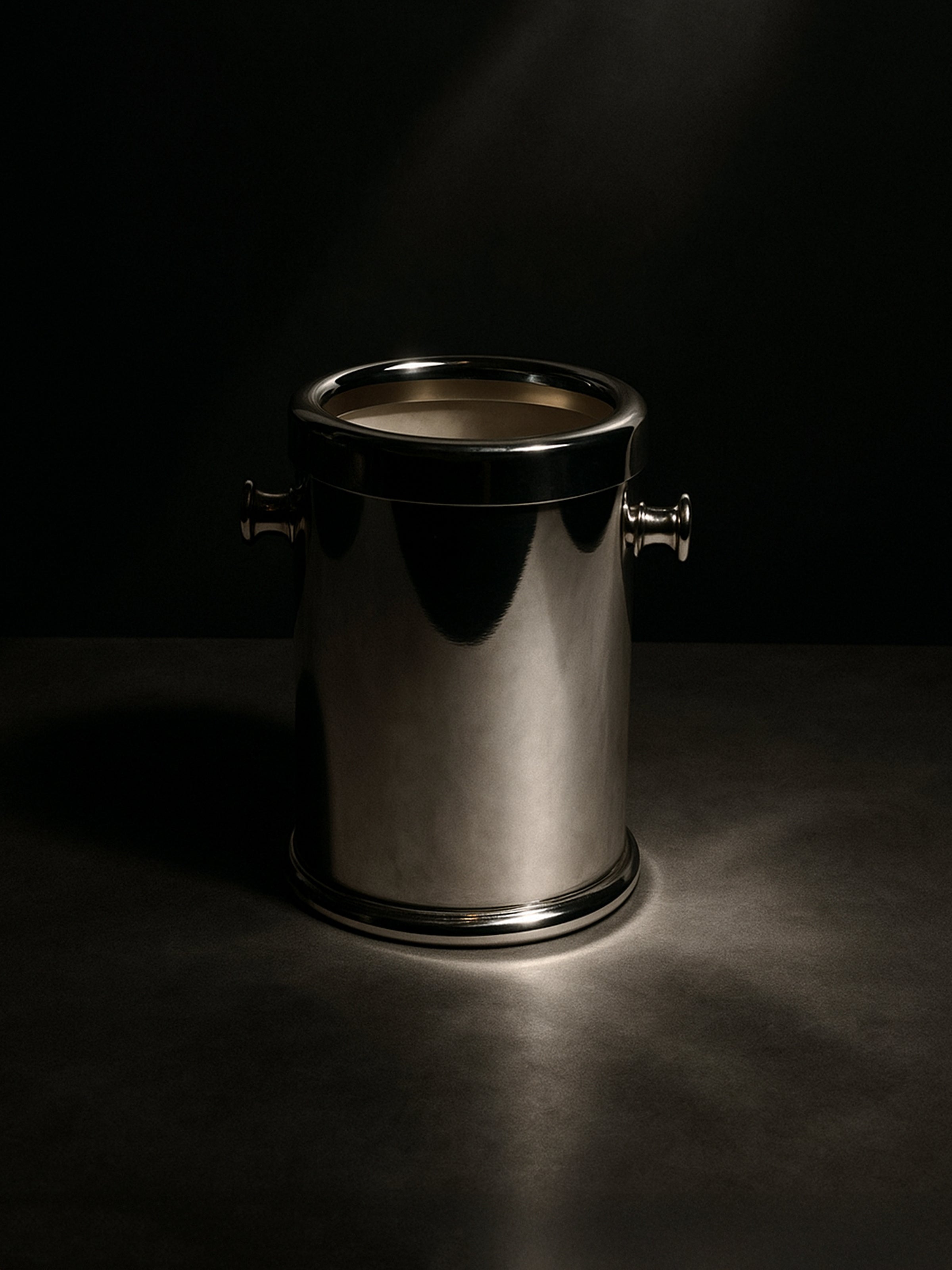 The Dodo Vintage Silver Plated Champagne Cooler - 1980s, featuring side handles, gleams under focused lighting on a dark surface against a black background.