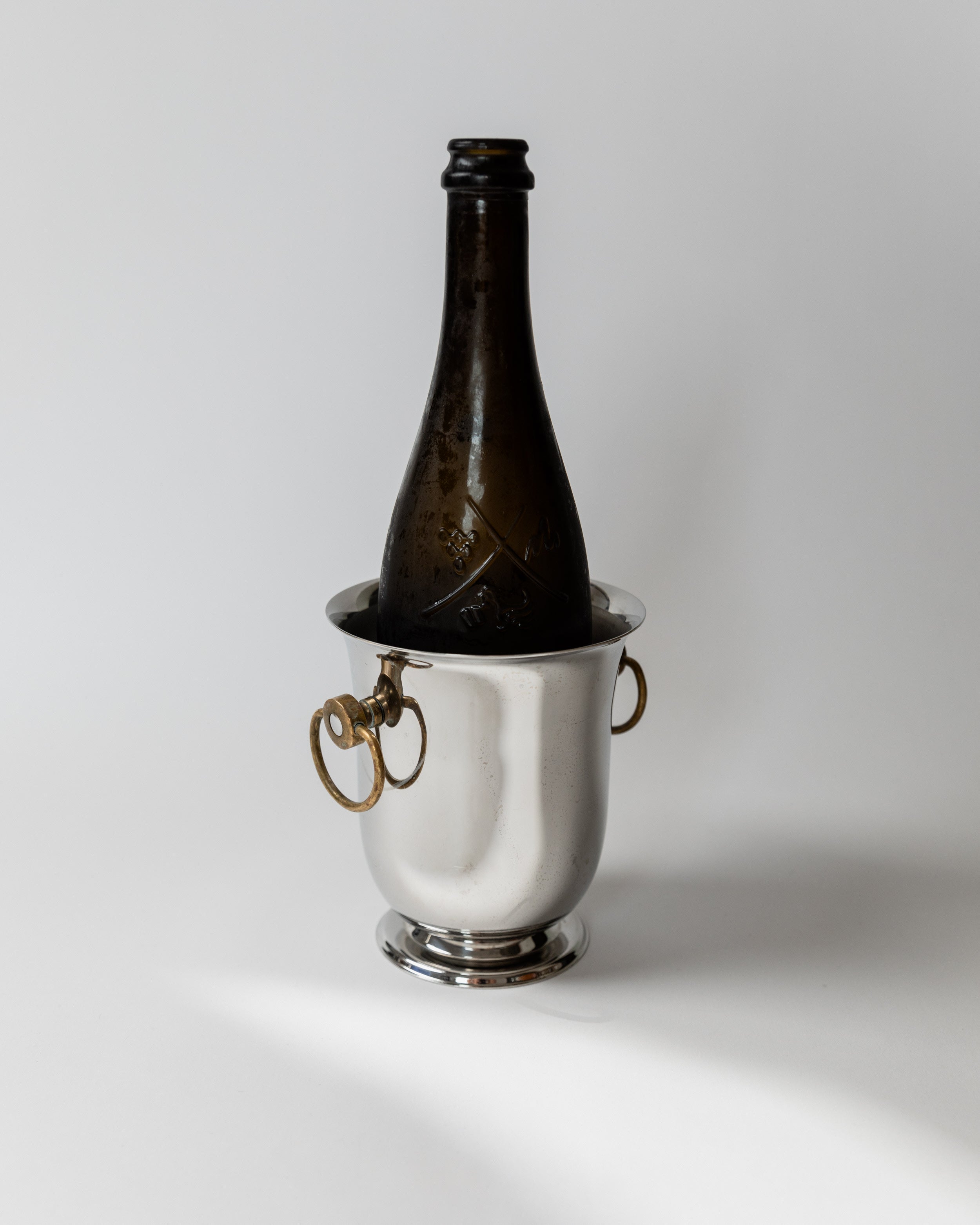 Silver champagne cooler with dark bottle and brass ring handles