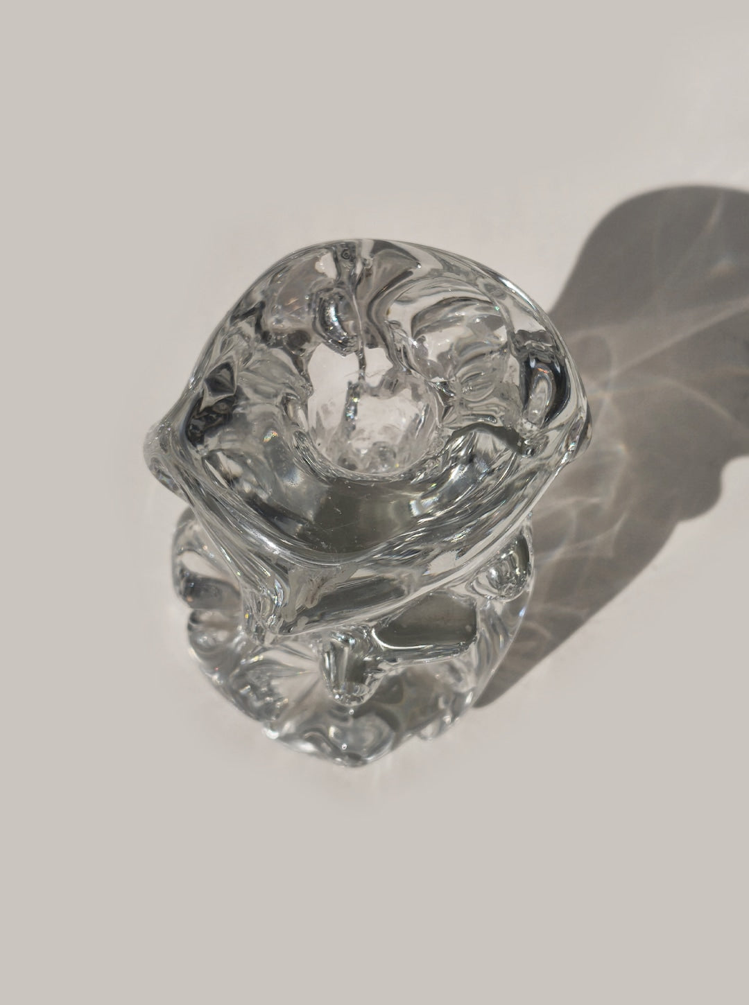 The Les Objoies Organic Glass Candle Holder, with its biomorphic design, rests on a light surface and casts a soft, intricate shadow featuring wavy patterns.