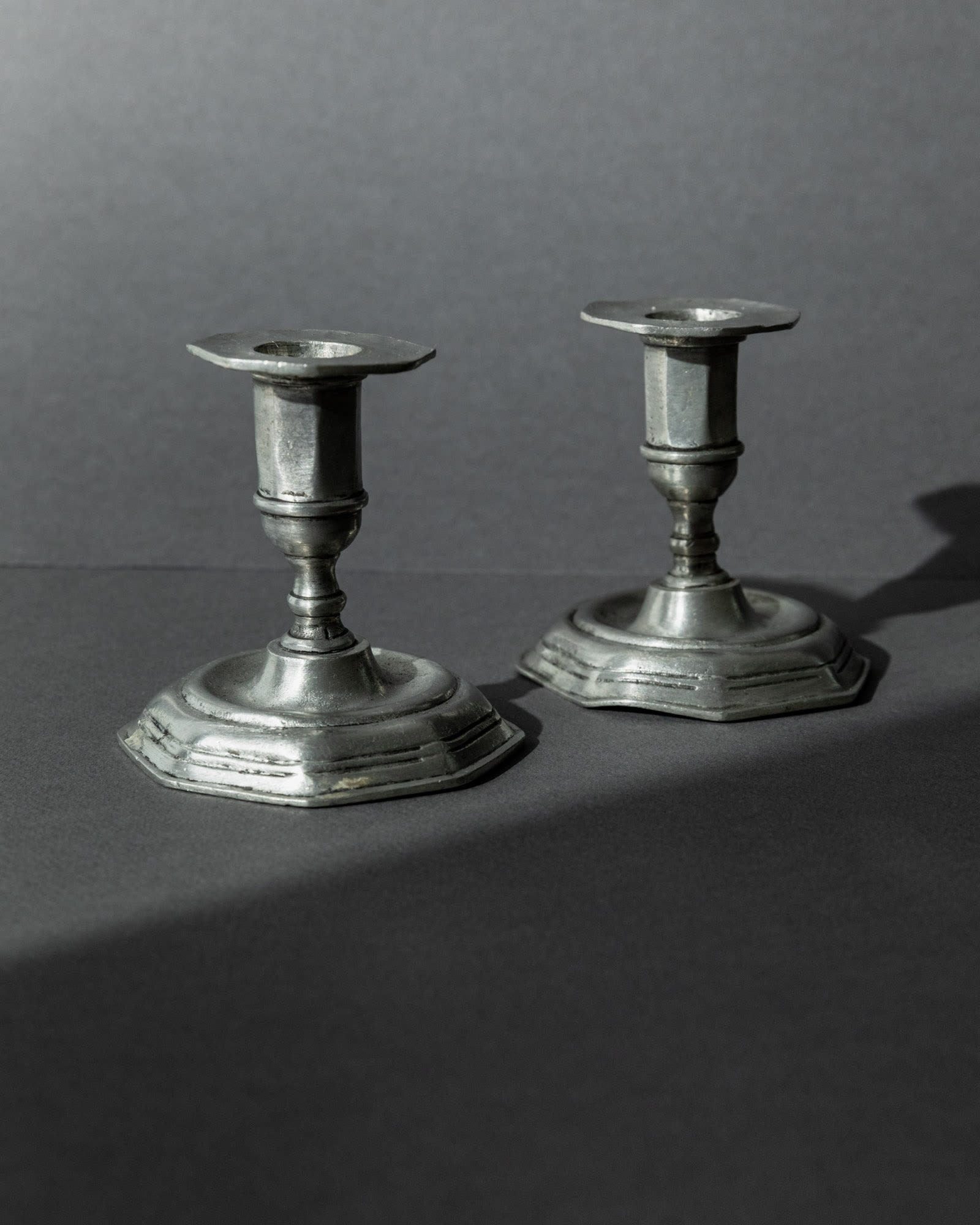 1900s Pewter Candleholders Set of 2 — angled view on dark background