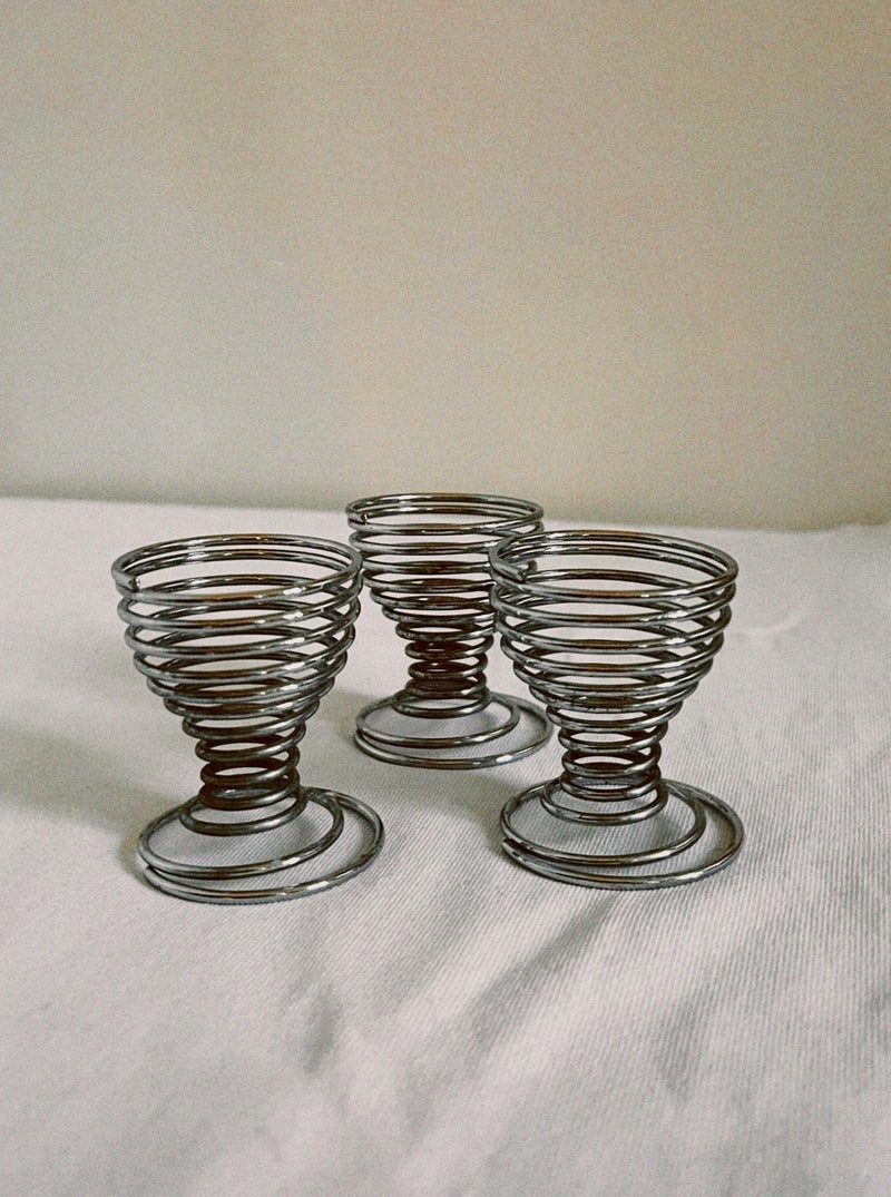 The Manushi Swirl Egg Cup Set features three empty, spiral-shaped egg cups arranged on a white surface with a light background—ideal for elevating your breakfast tableware collection.