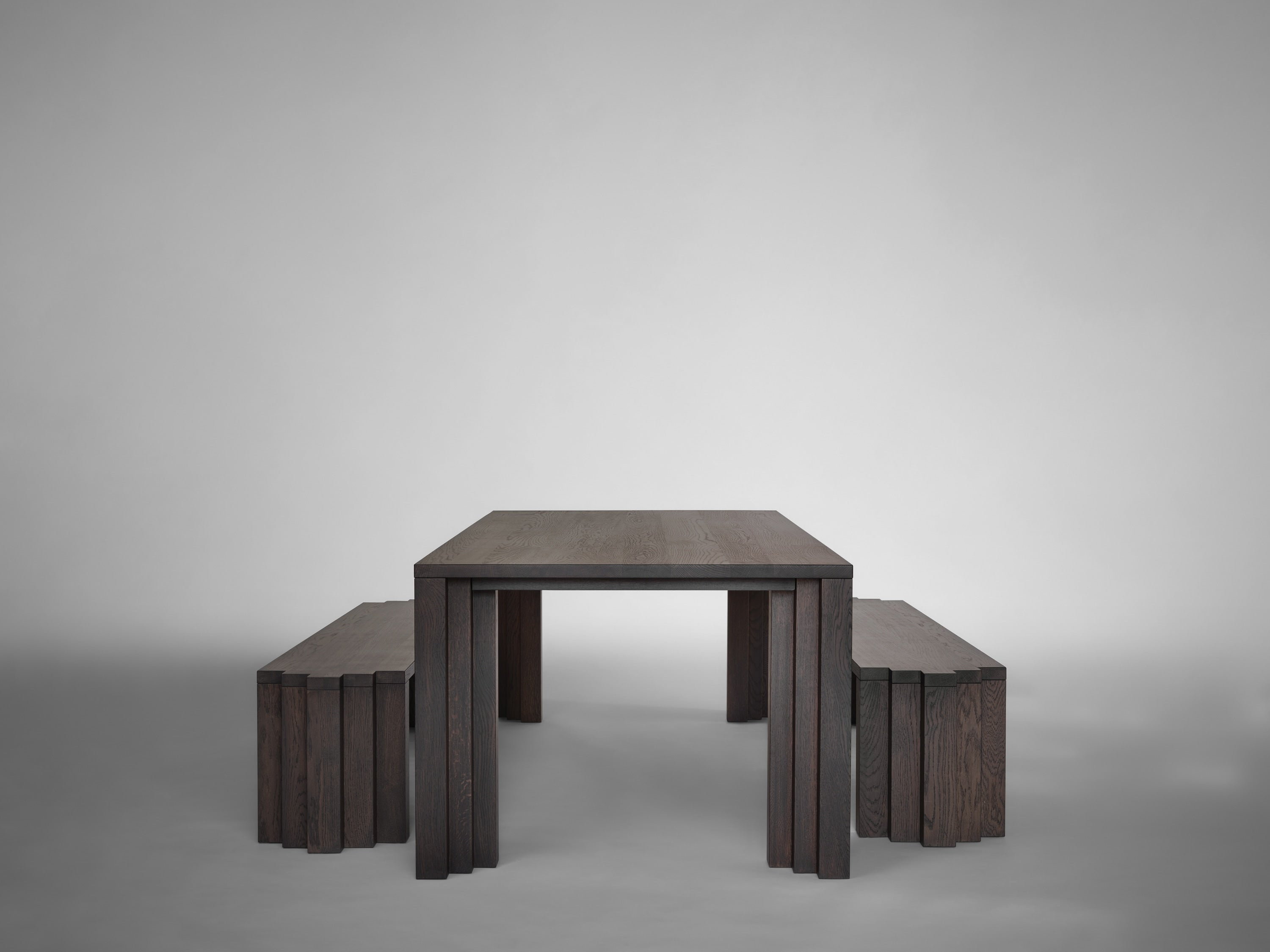 A minimalist dark wooden dining table of solid European oak is paired with Mokko Cadence Benches on either side, all set against a plain light gray background.