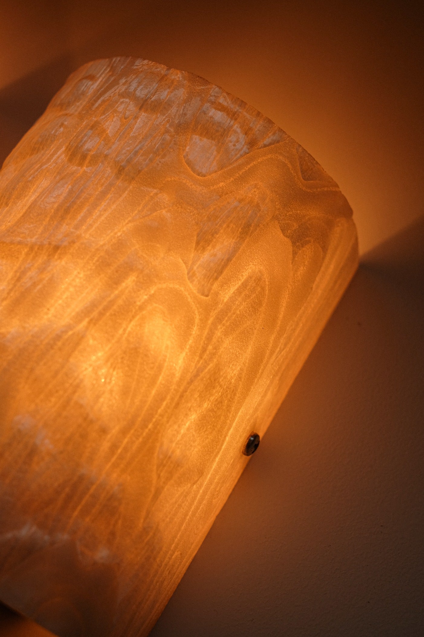 A close-up of a septembre studios Set of 2 Mother-of-pearl Wall Lamps, featuring textured, translucent shades that cast a warm, ambient glow on a neutral wall.