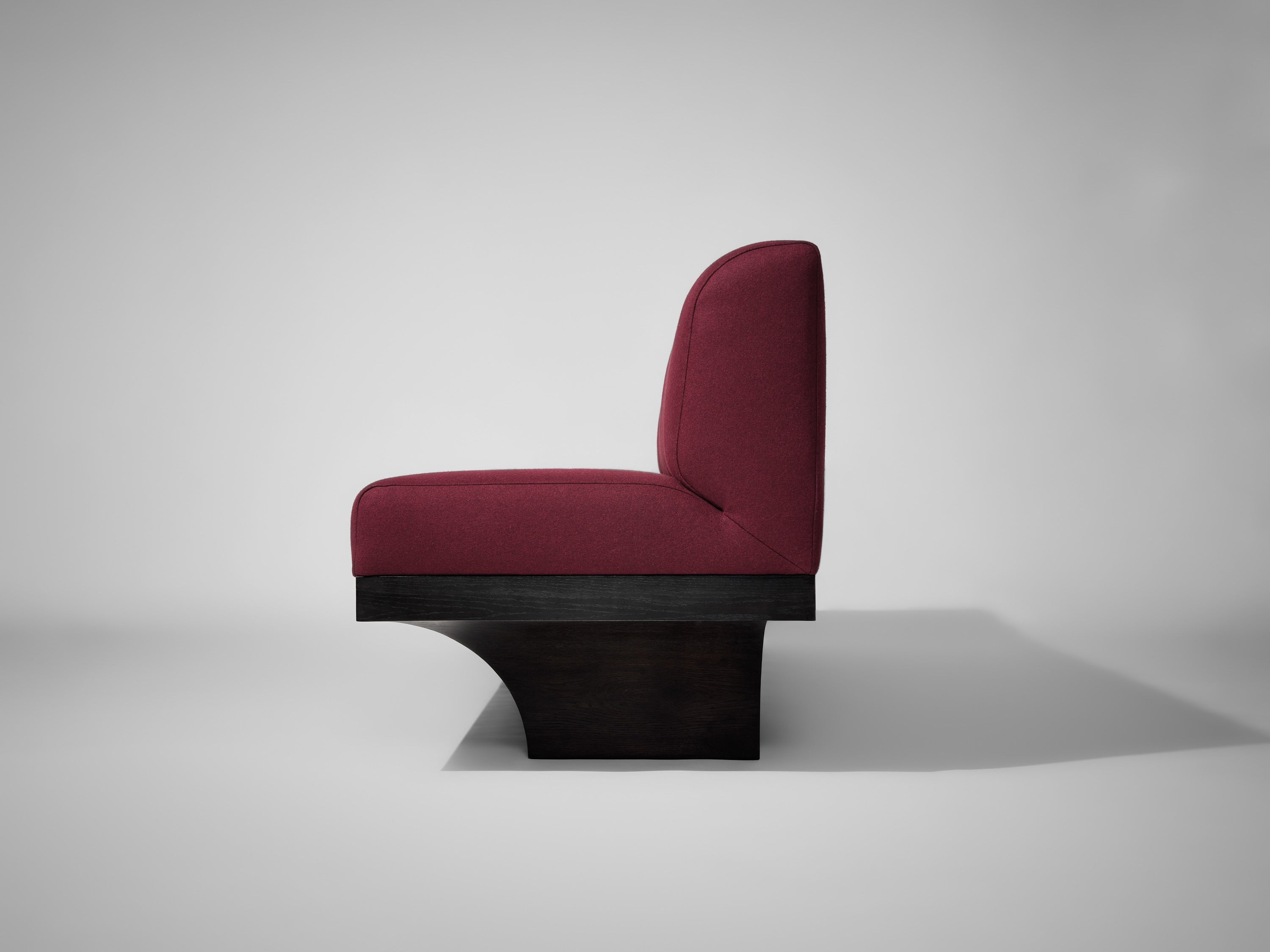 A side view of a modern chair with a burgundy upholstered seat and backrest, featuring a unique black wooden base, is shown against a light gray background—ideal for pairing with the Mokko Acer Sofa.