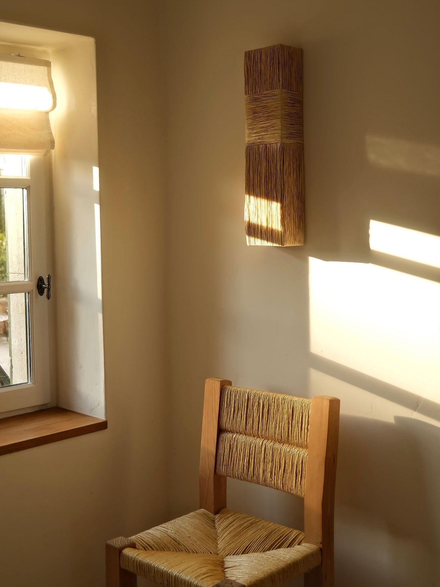 Eliane Wall Sconce in raffia — mounted on wall beside wooden chair