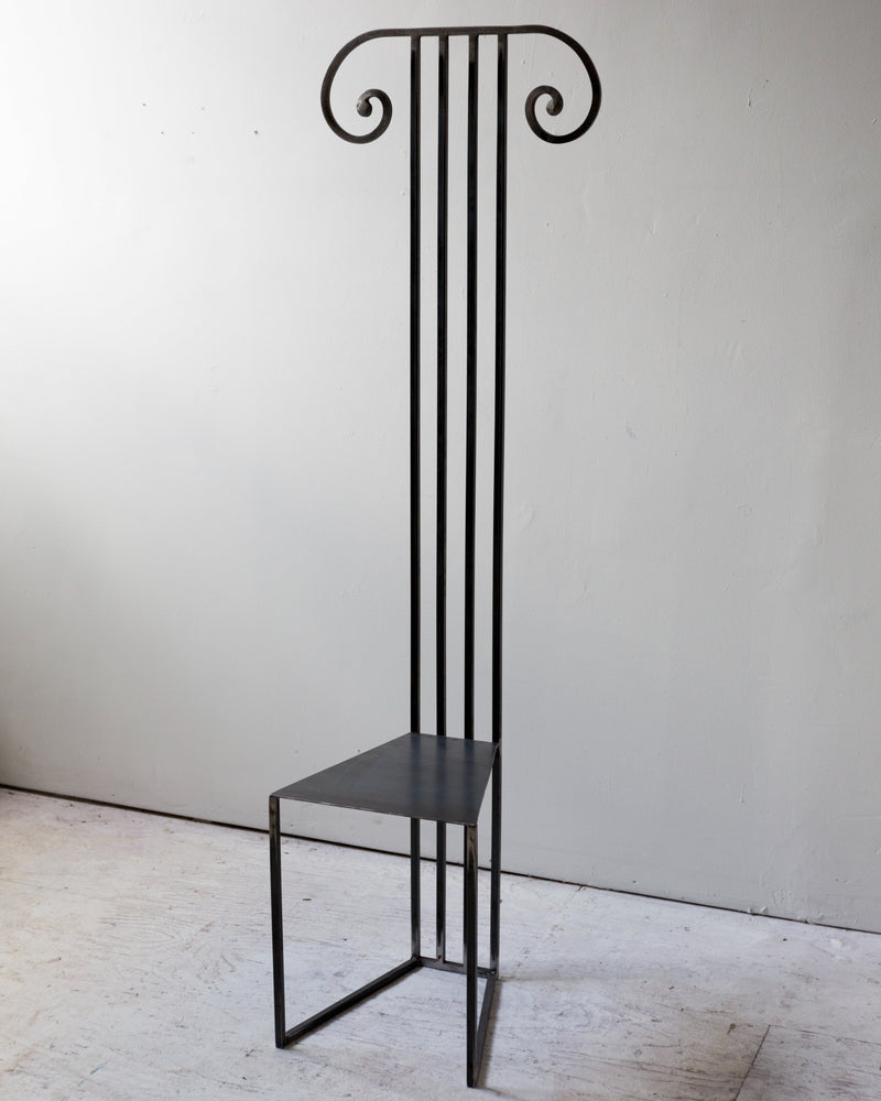 High-back black metal chair with decorative scrolled top and minimal seat