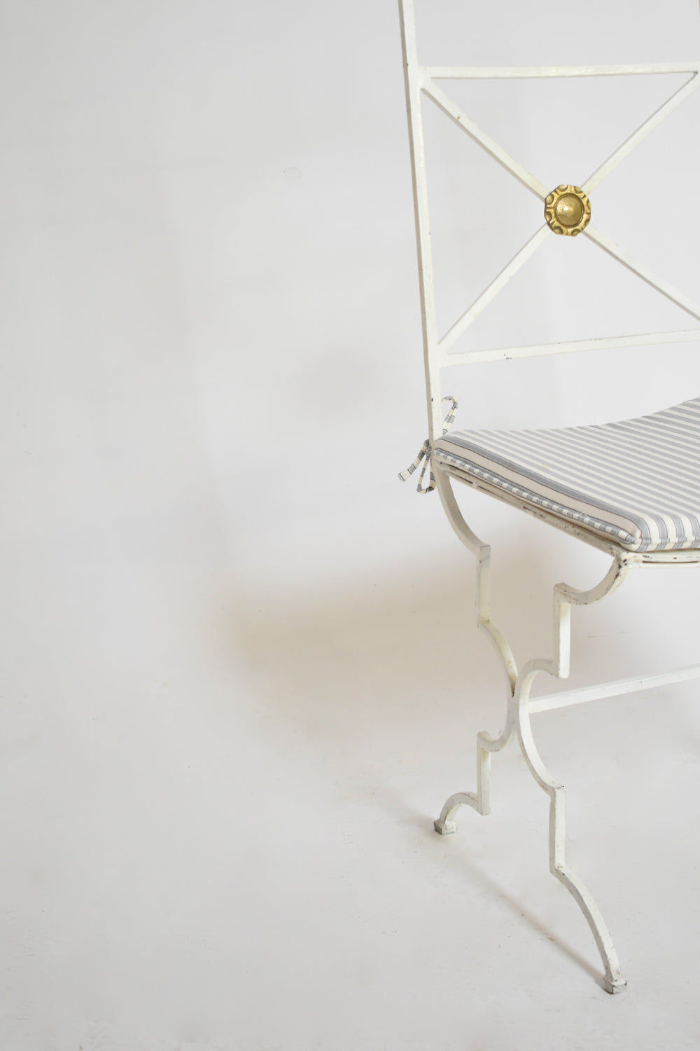 This elegant Barracuda Interiors set of four white wrought iron chairs from the 1940s features gold medallions on the backrests and gray-and-white striped cushions, shown partially against a plain white backdrop.